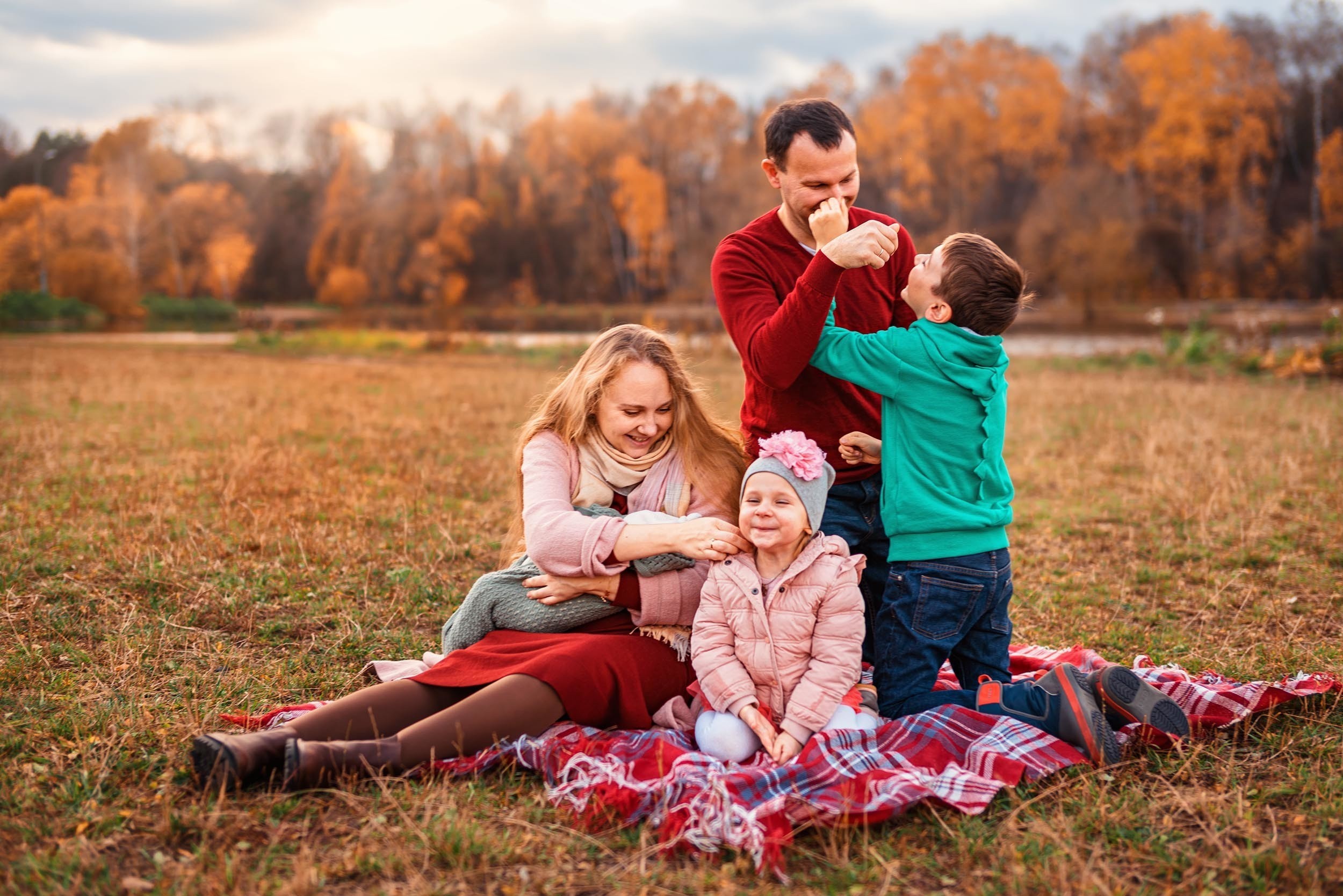 Семья играет на пледе посреди поляны на фоне осеннего леса и заката