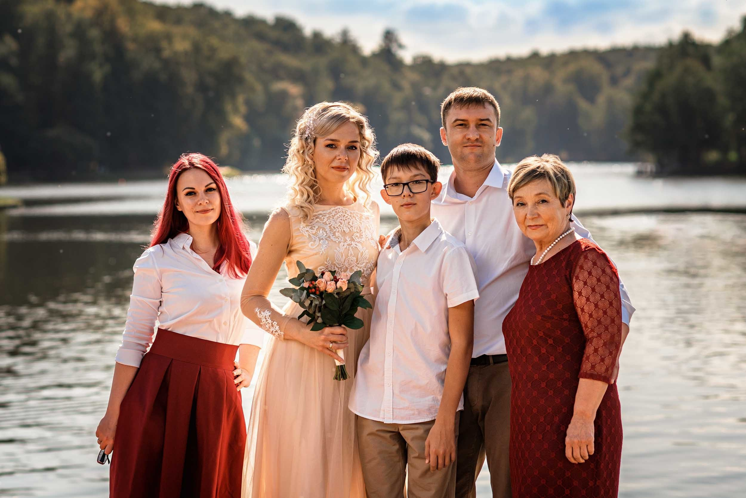 Молодожены с гостями стоят на берегу водоема