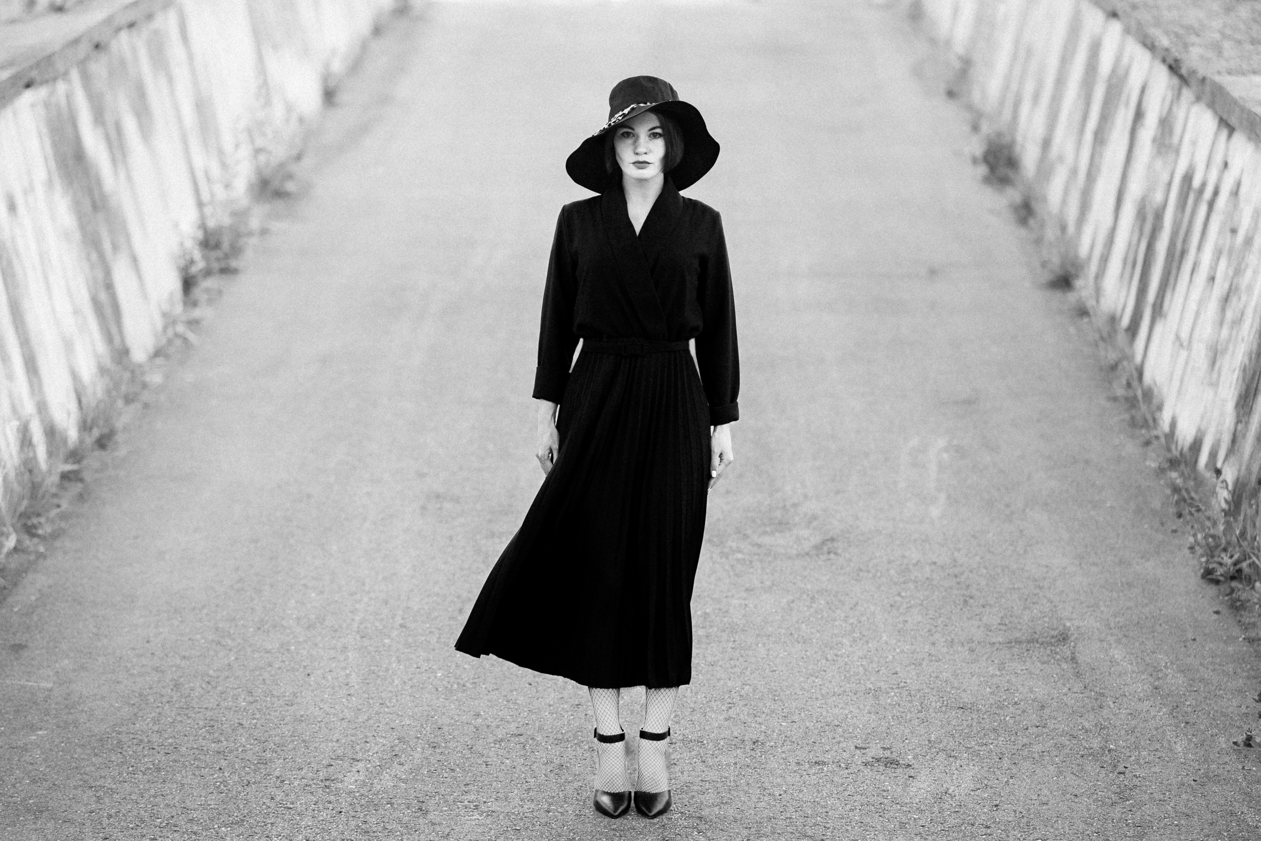 Женщина в чёрном платье и шляпе стоит на пустой улице, чёрно-белая художественная фотография в минималистичном стиле