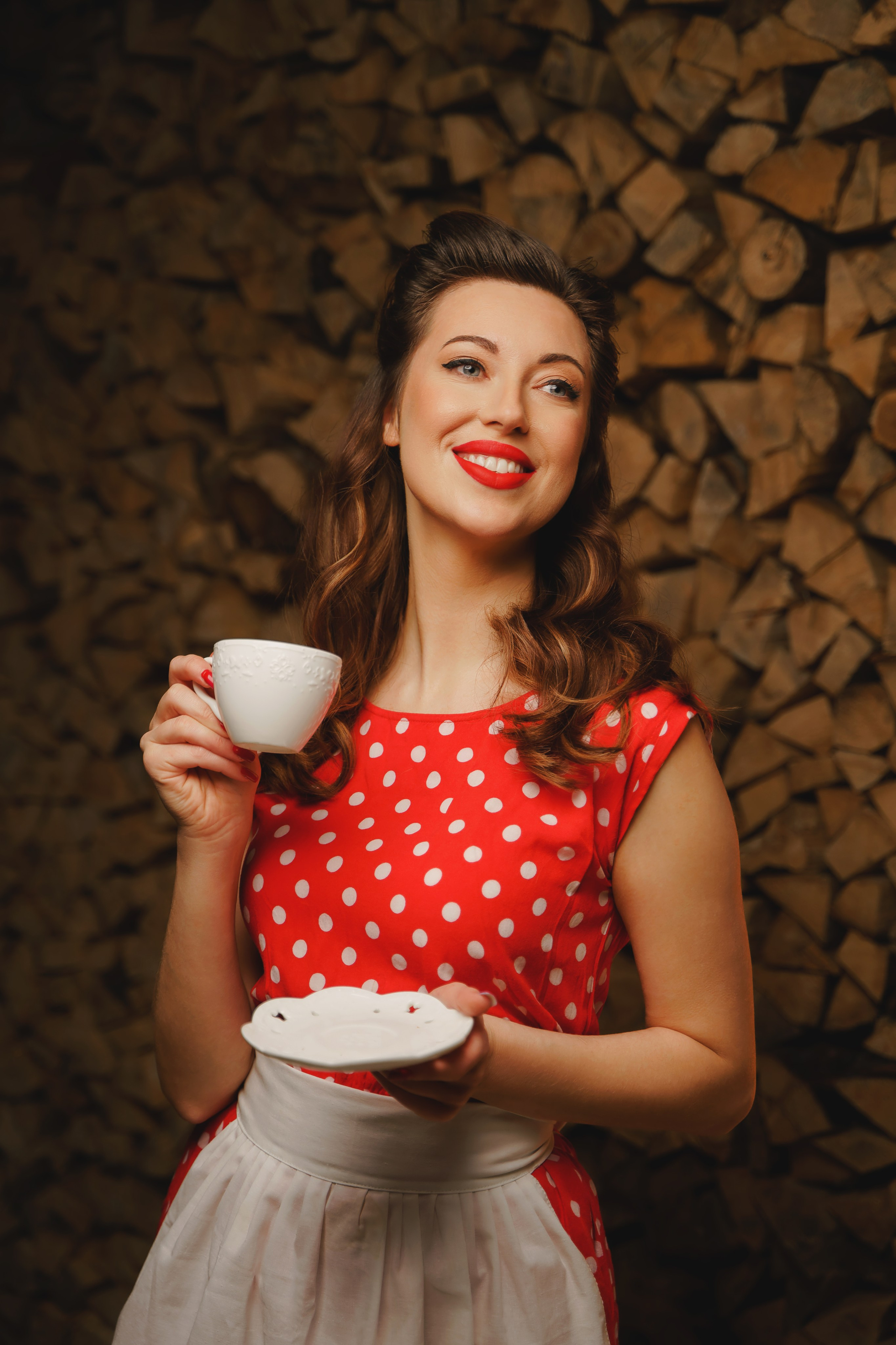 Веселая девушка в красном платье, держит в руках чашку кофе.