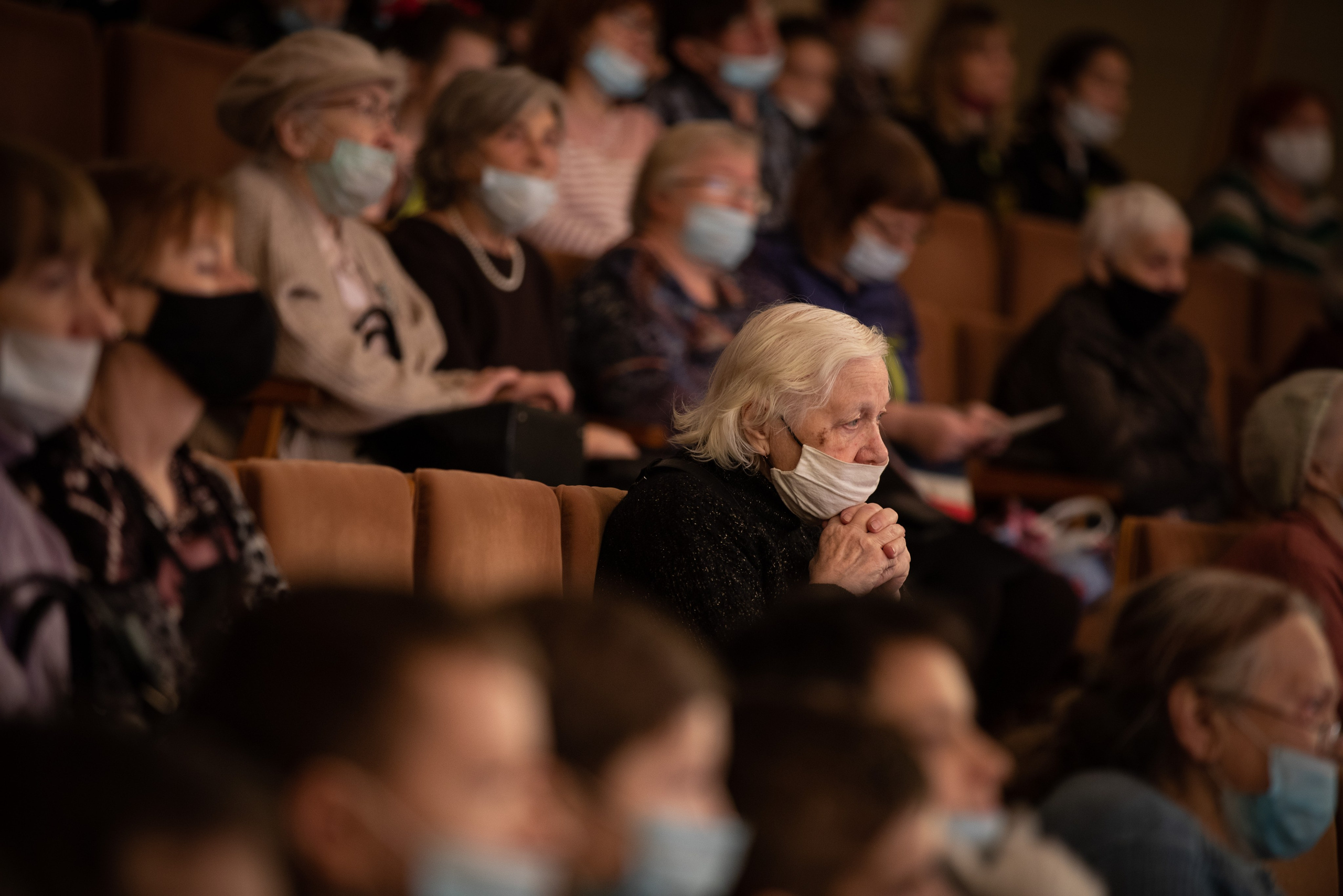 Пожилая женщина в маске в зрительном зале на концерте.