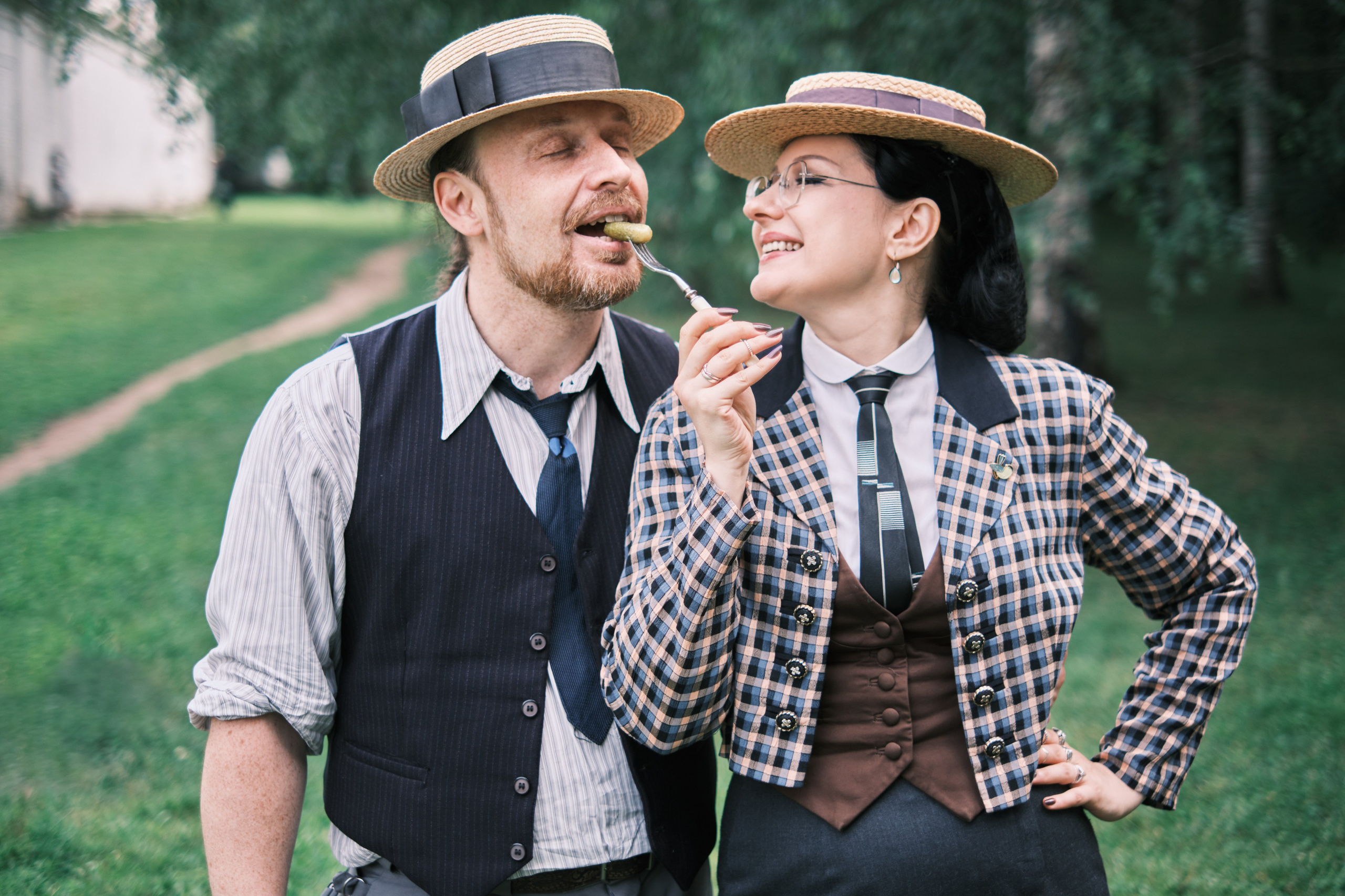 Девушка кормит мужчину огурчиком на вилке оба в соломенных шляпах