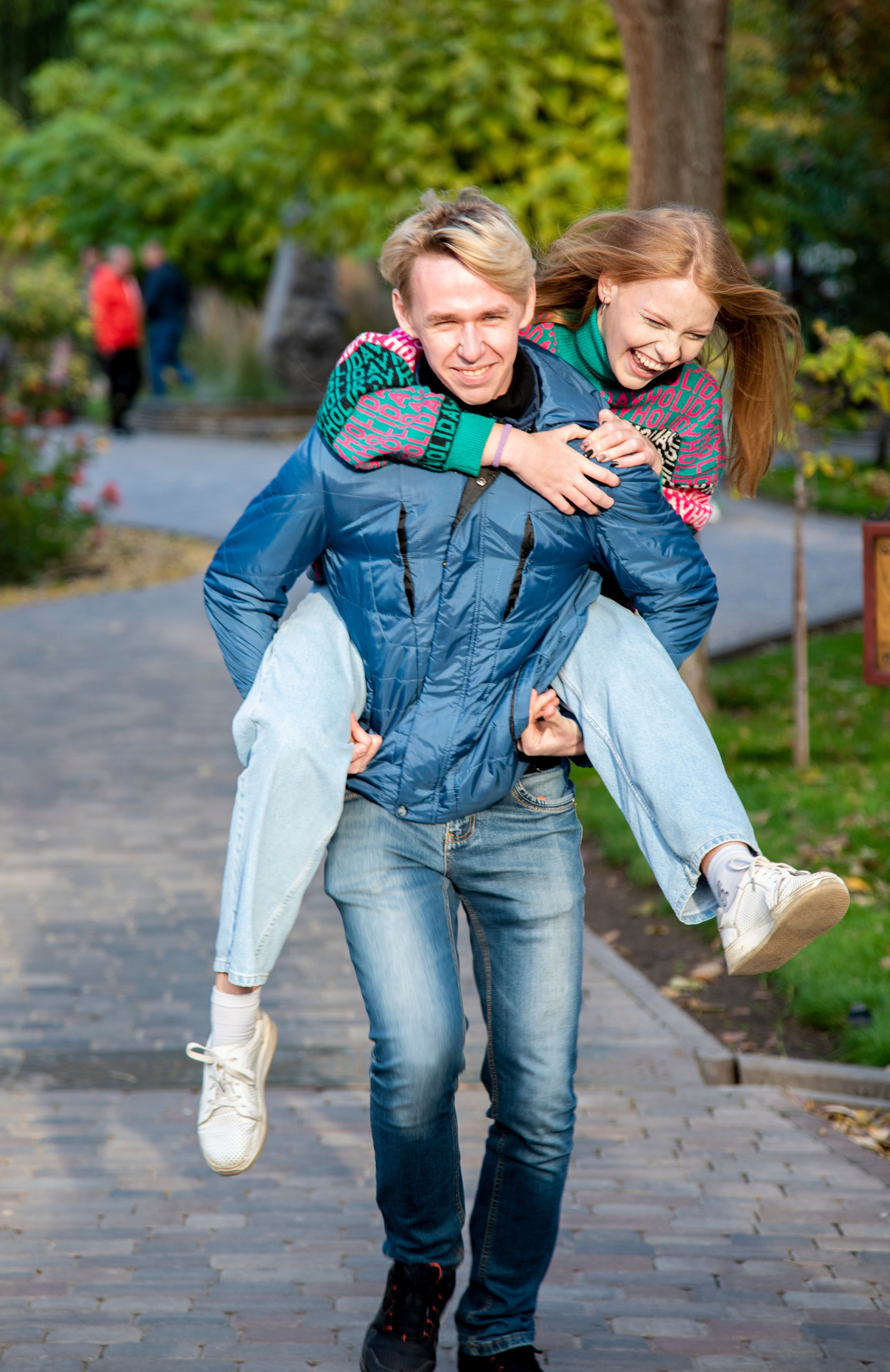 молодая девушка студентка. блондинка. длинные волосы. розово-зелёный свитер. парк Лога . осень брат с сестрой. парень несёт девушку