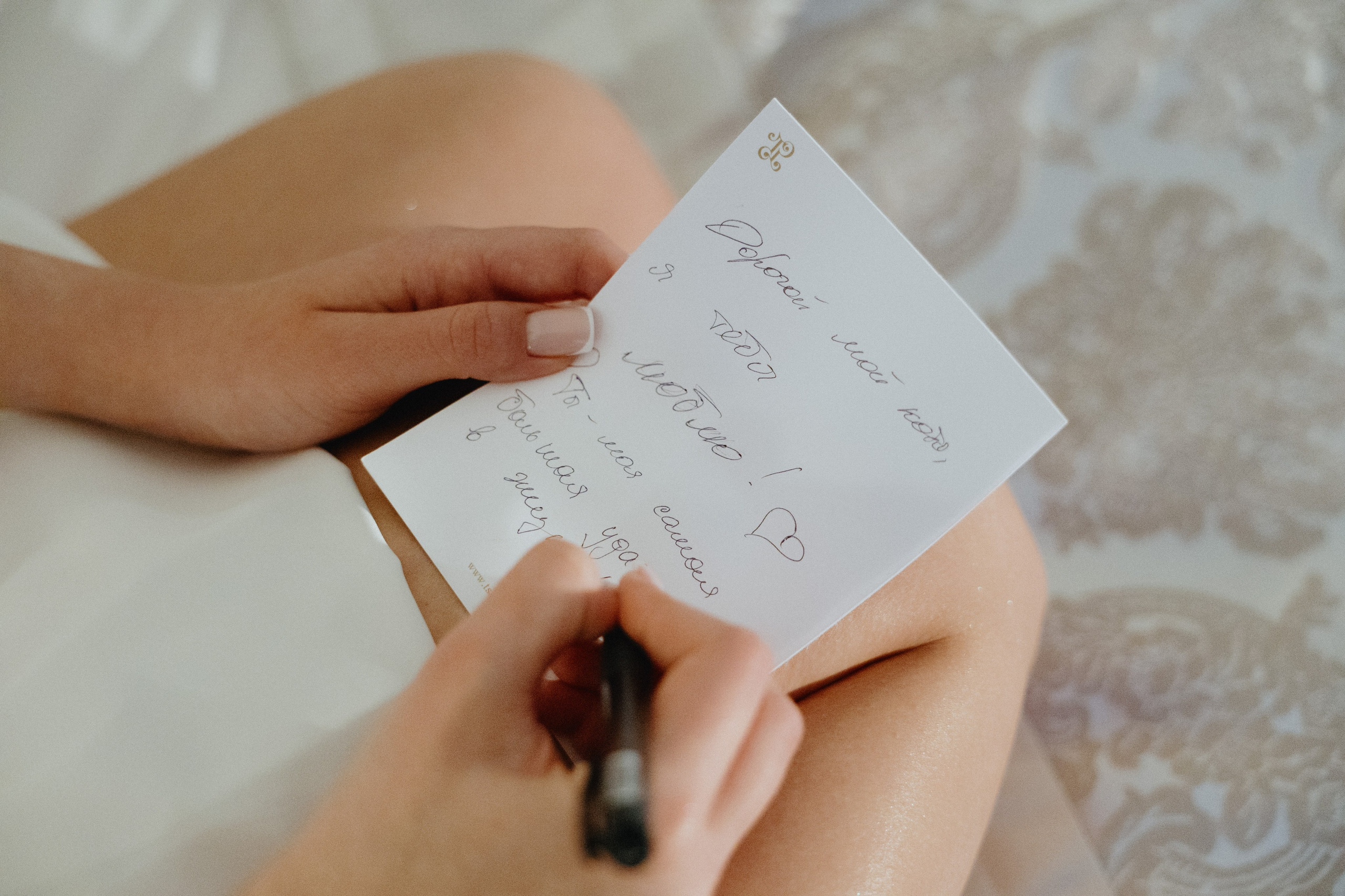 Женская рука держит открытку и пишет на ней ручкой.