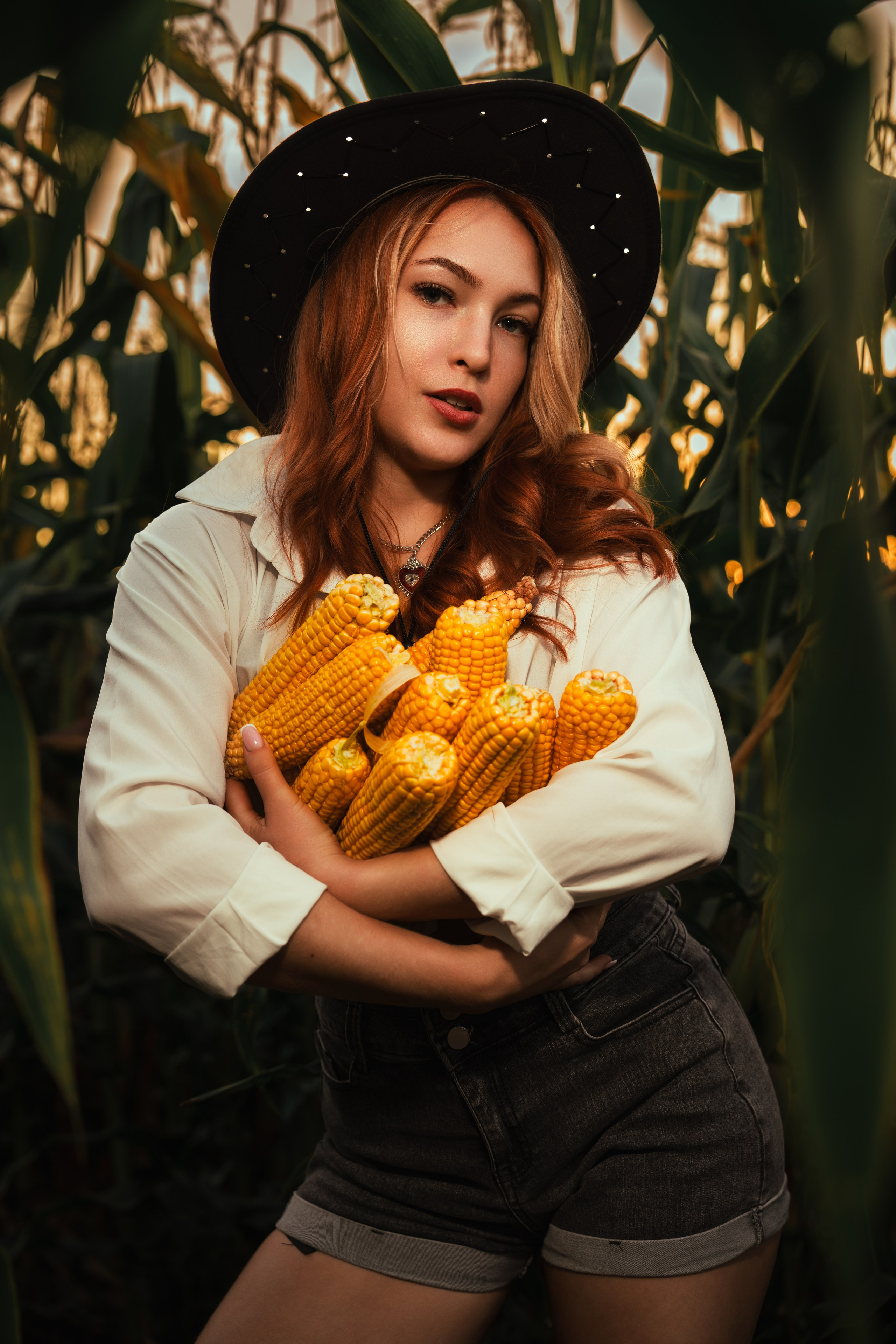 девушка фермер стоит в шортах и шляпе в поле с кукурузой