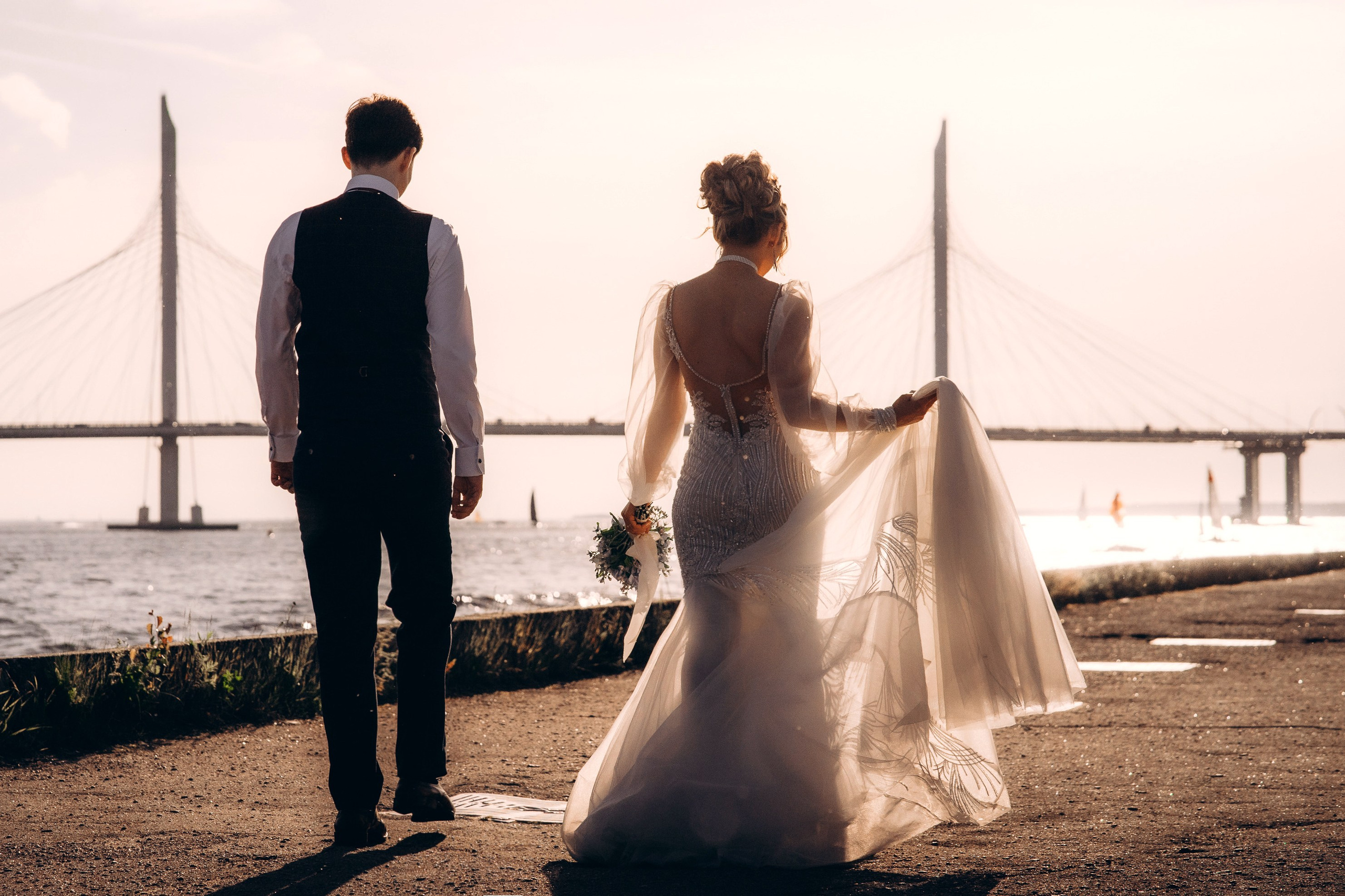 жених и невеста идут спиной на закате на набережной 