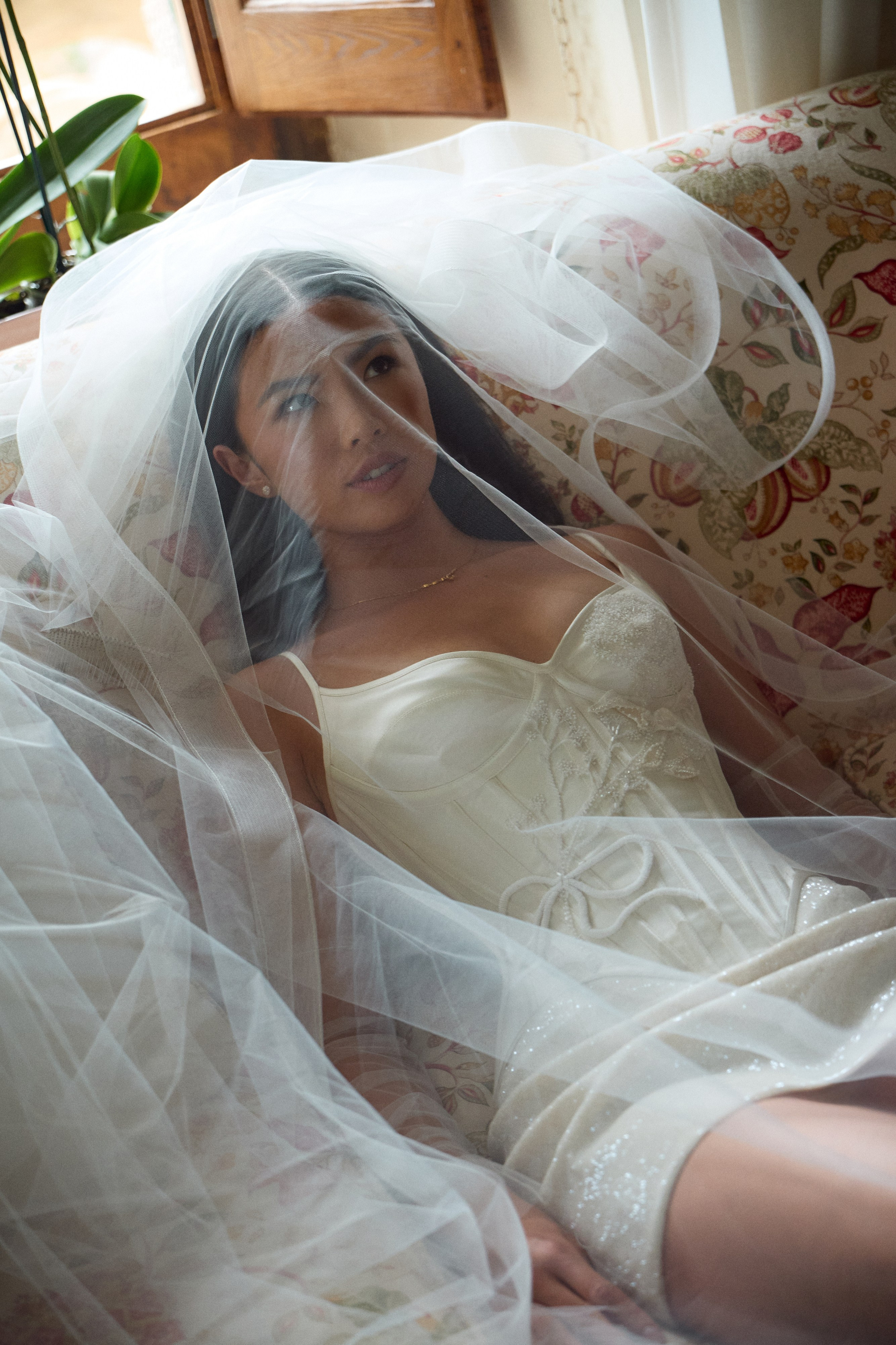 Bride reclining on a floral sofa beneath her veil