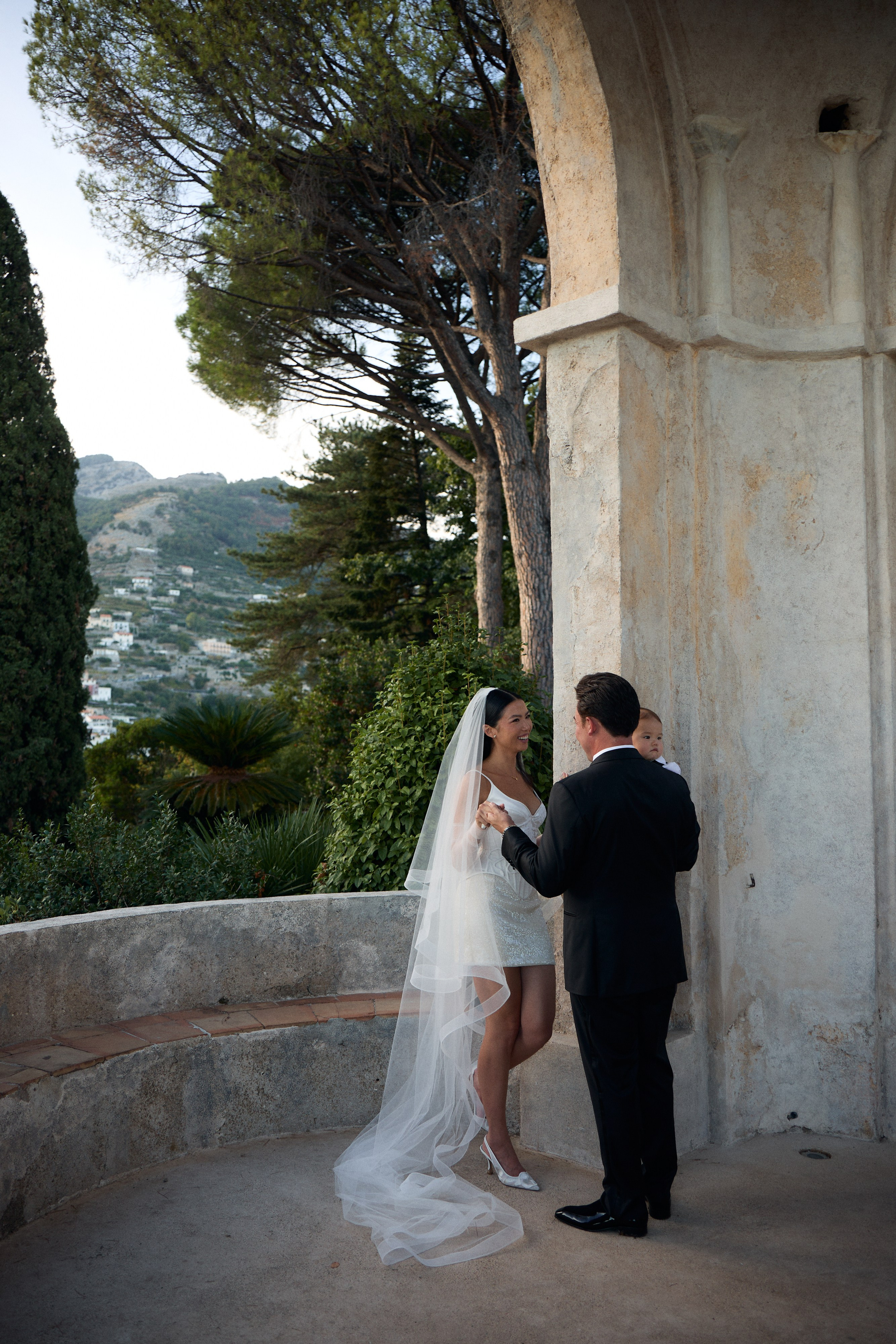 Bride and groom together beside a stone arch overlooking the sea