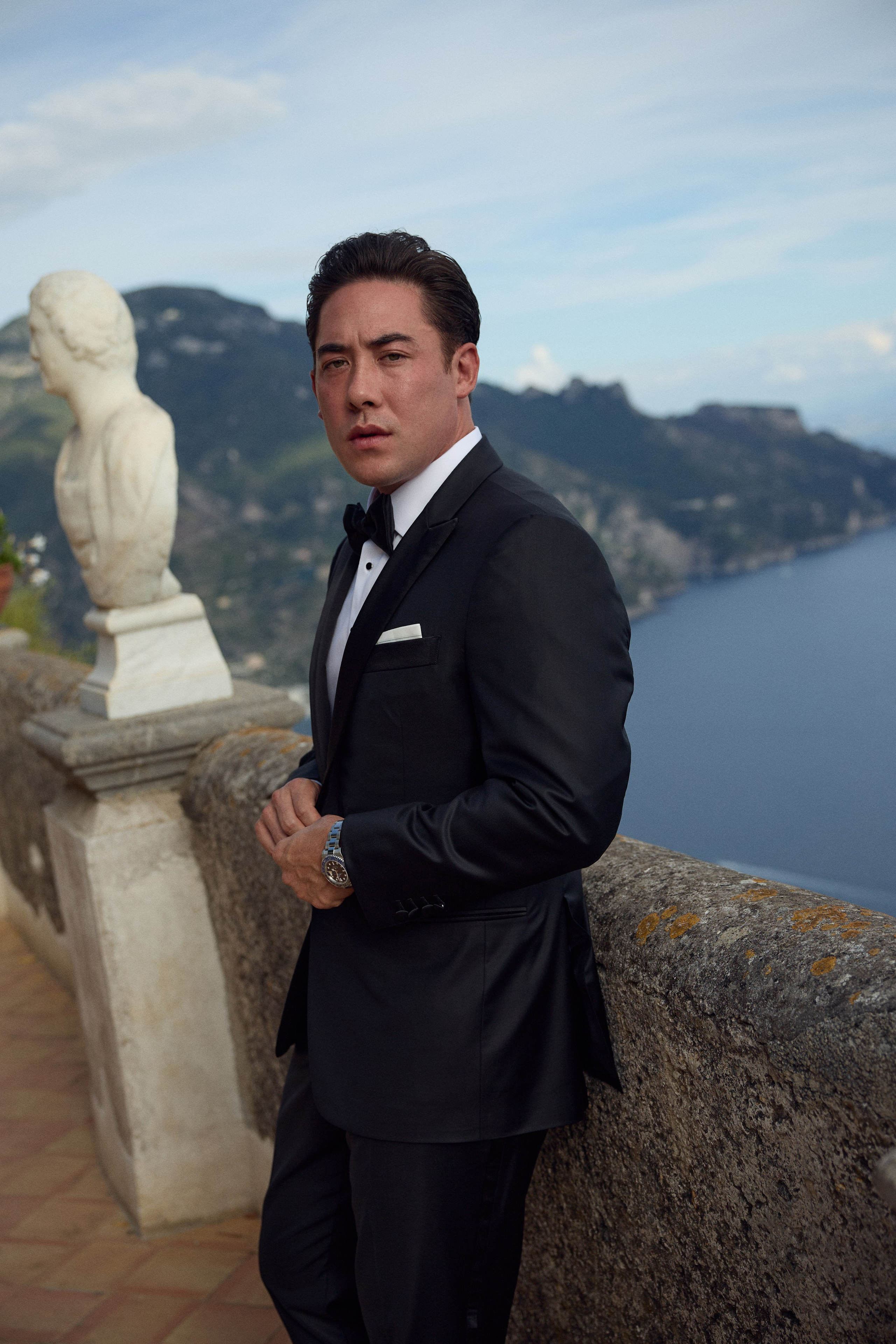 Groom in a black tuxedo beside a marble bust on the Terrace of Infinity