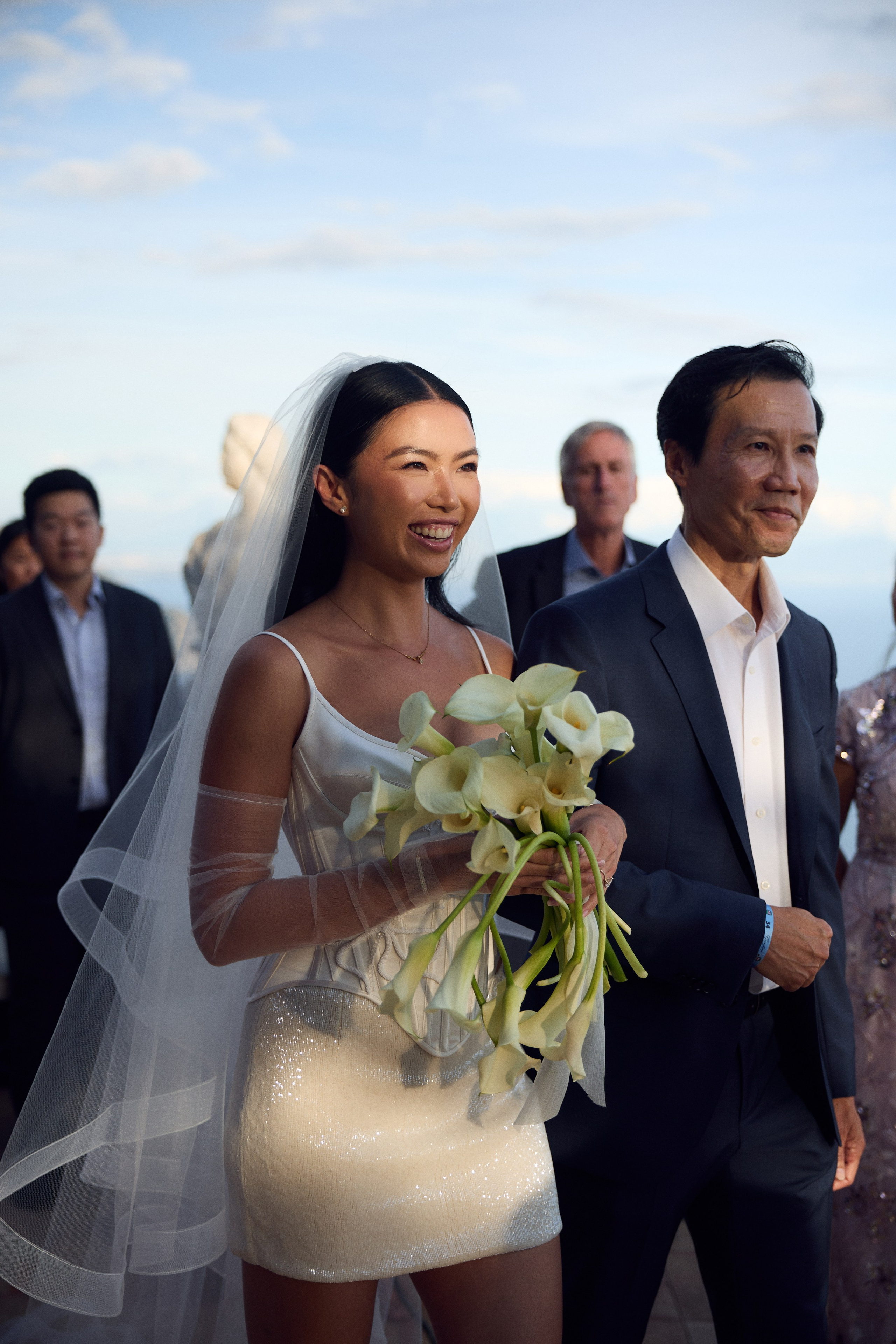 Bride smiling with a calla lily bouquet as she walks down the aisle