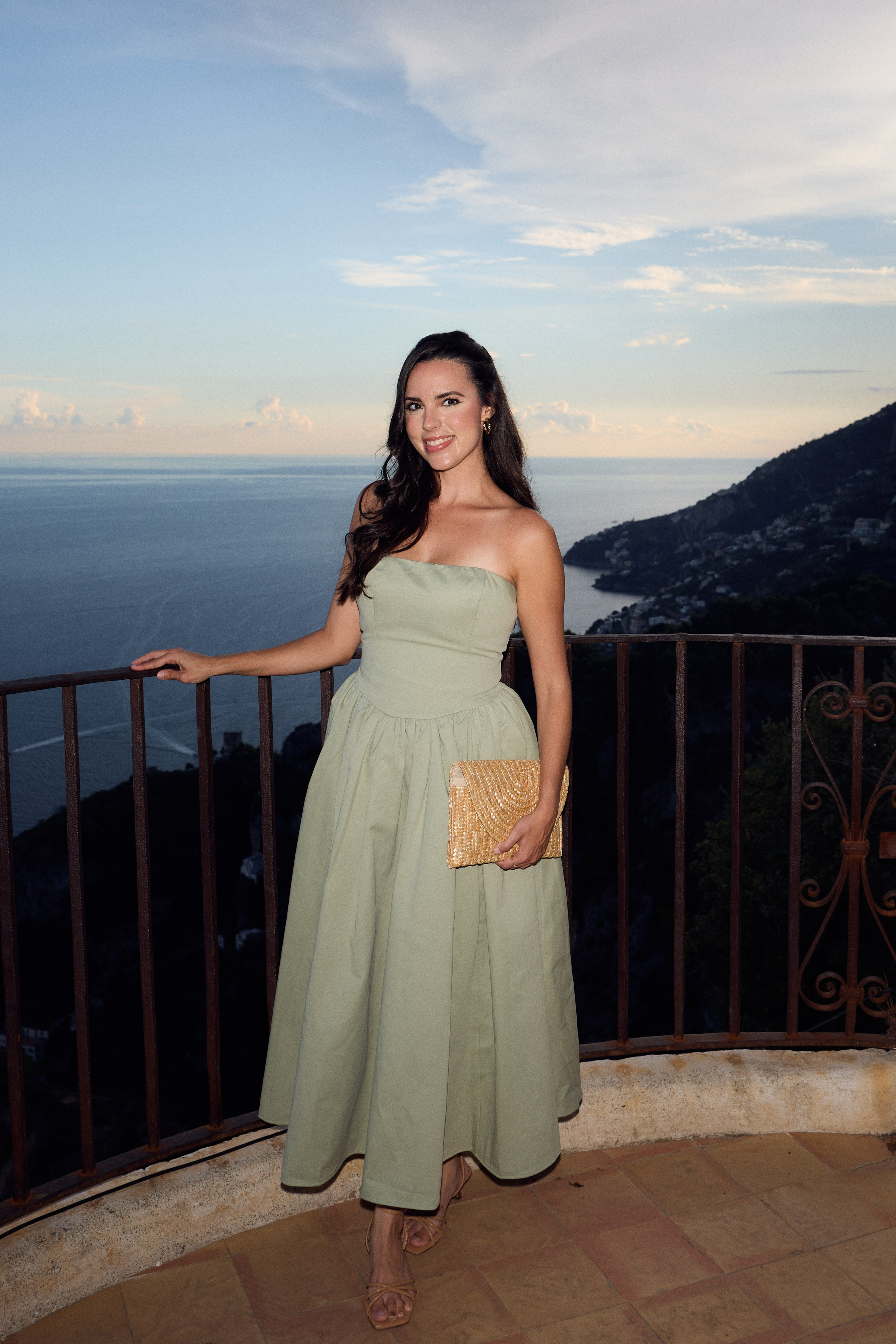 Wedding guest in a green dress on a terrace overlooking the sea