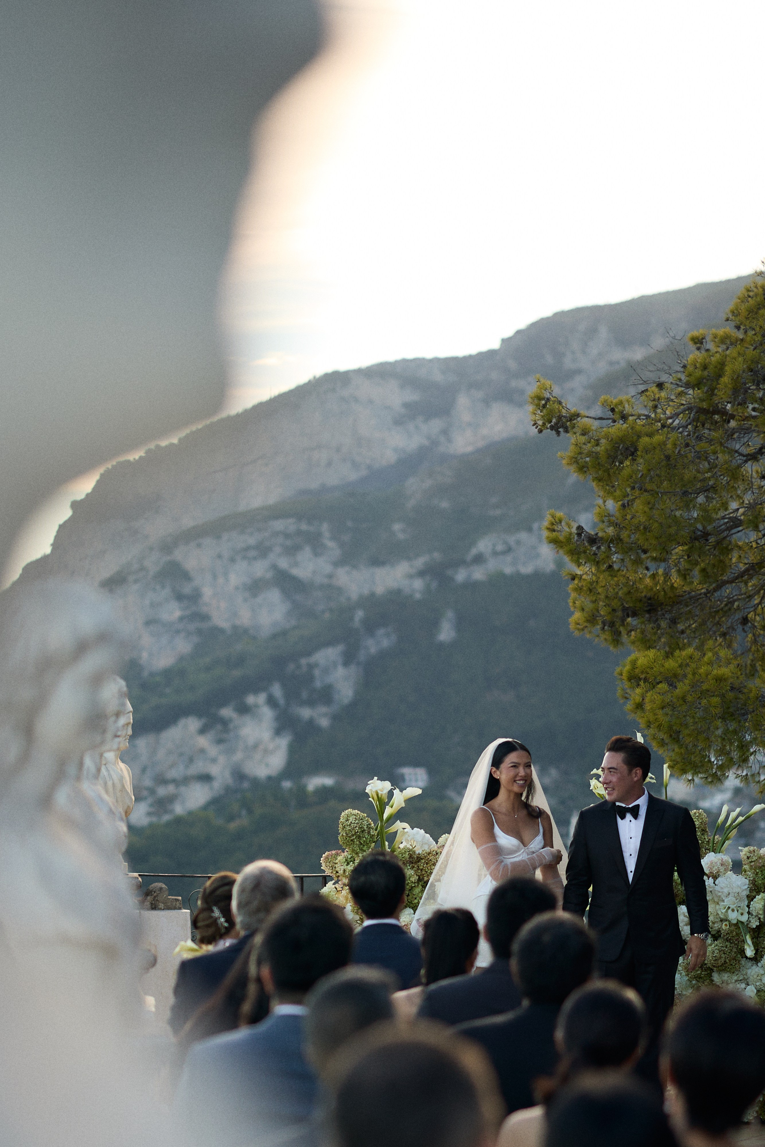 Wedding ceremony overlooking the sea, framed by a marble statue