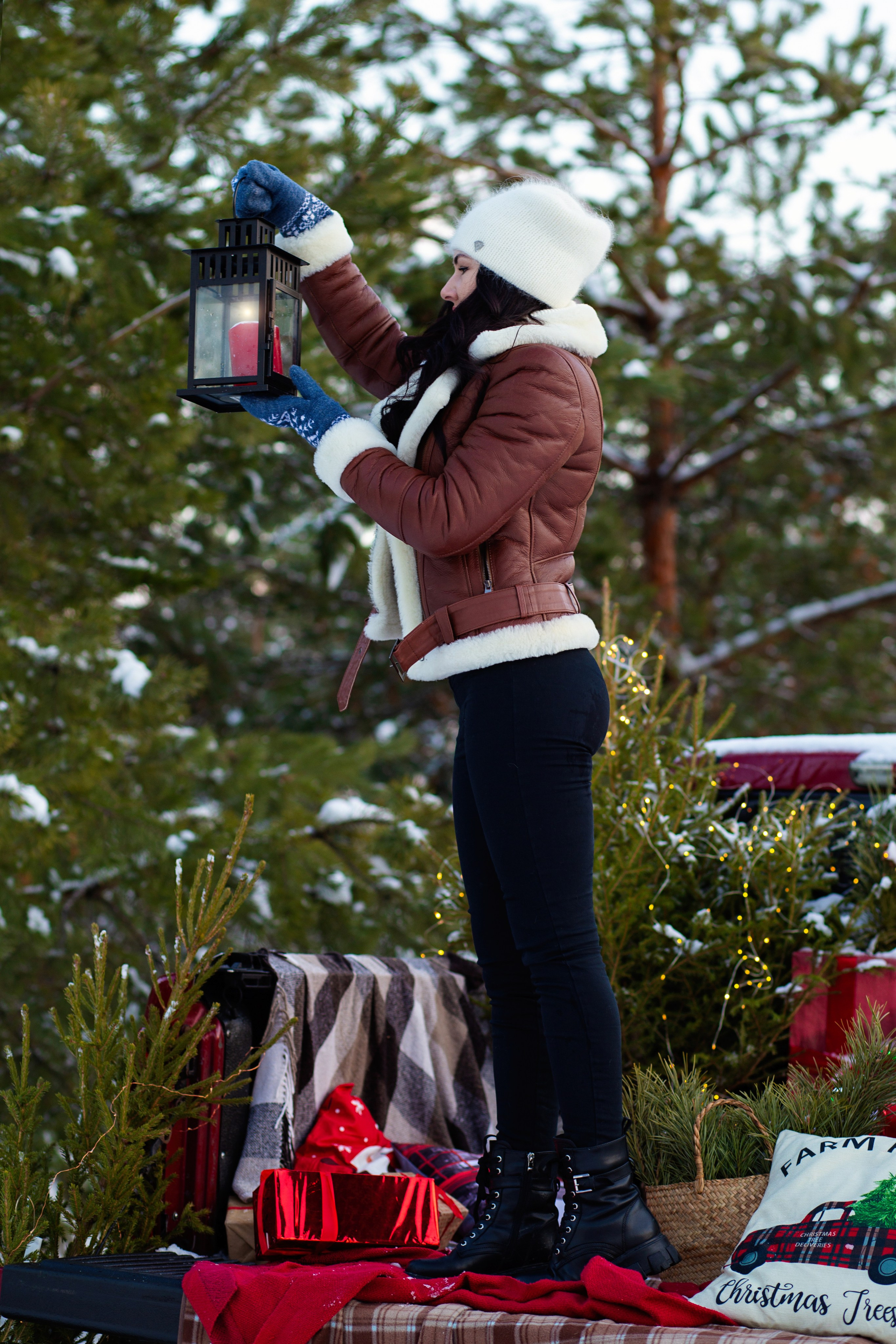 девушка   в коричневой   куртке  стоит в    машине пикап красного цвета и  из кузова наряжает  елку  в лесу 