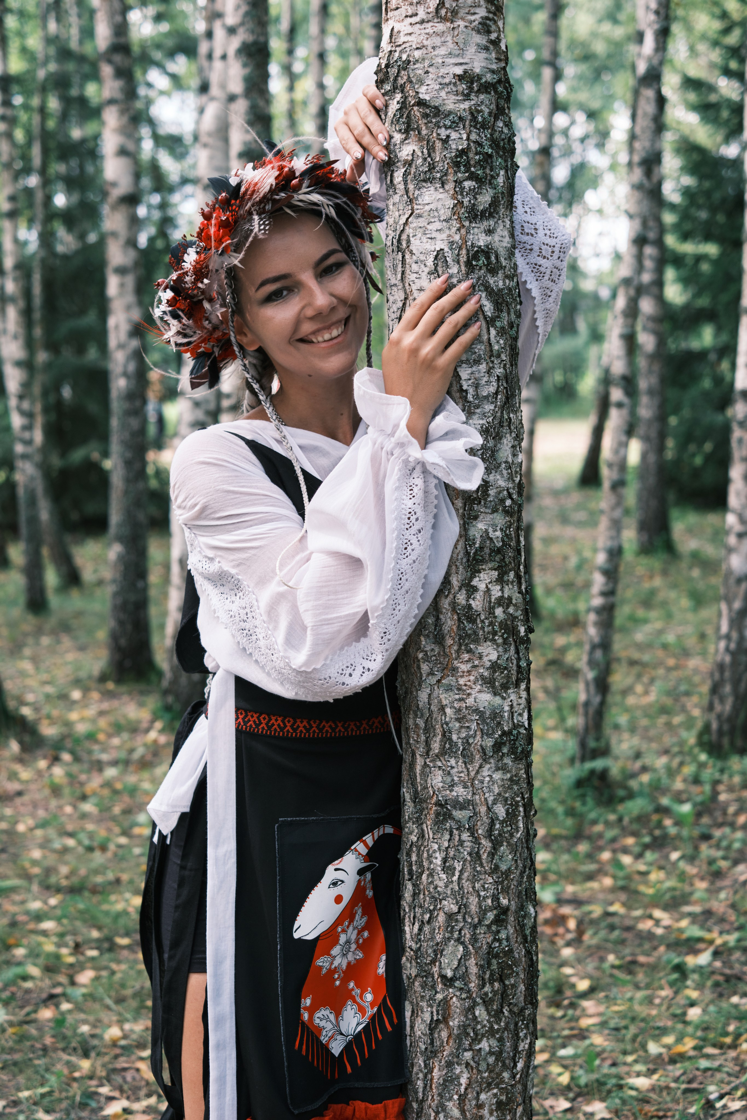 Девушка в русском костюме с венком на голове обнимает березу
