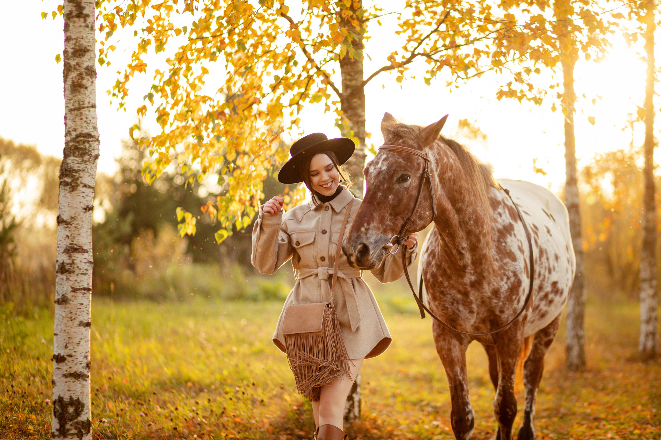 Девушка идет по залитому солнцем лугу, держа за поводья лошадь.