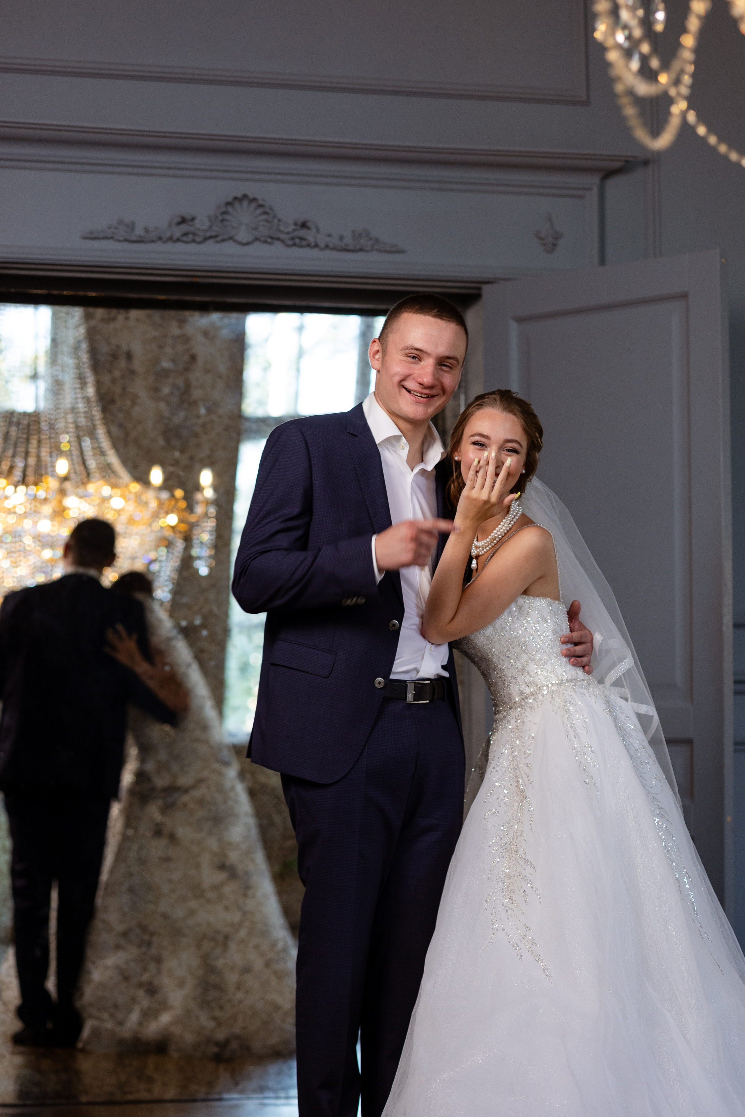 Улыбающиеся молодые стоят в обнимку, отражаясь в большом зеркале.