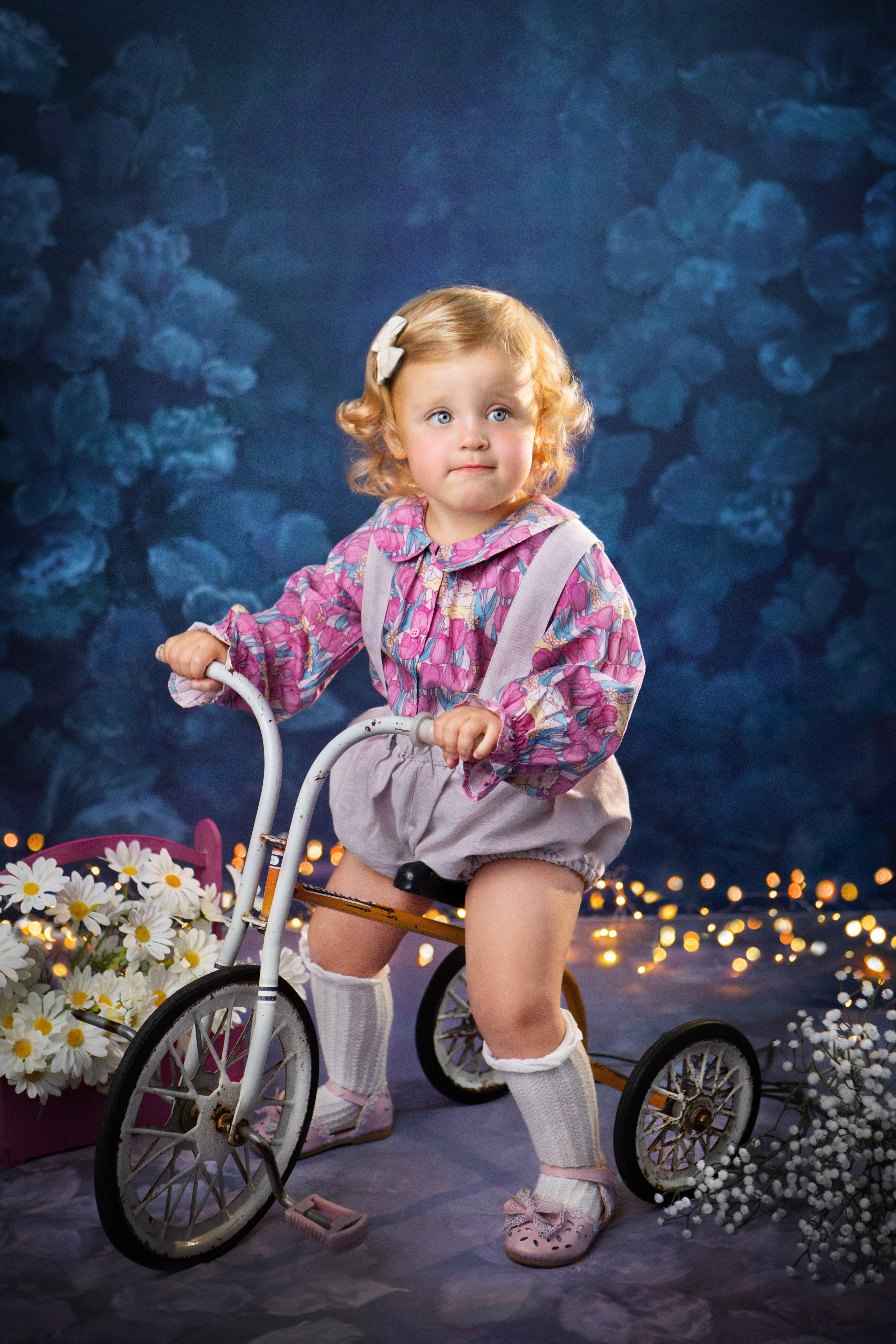 Белокурая малышка едет на ретро-велосипеде. Вокруг нее множество ромашек.