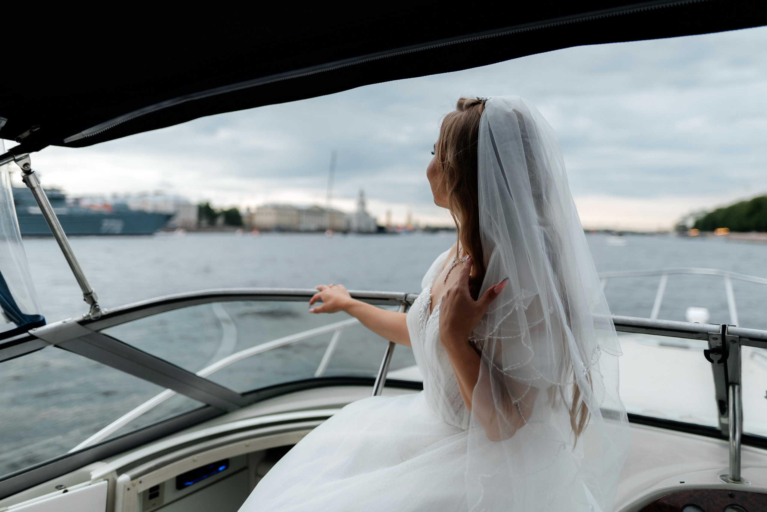 невеста на свадебной фотосессии сидит спиной к фотографу на яхте в акватории Невы