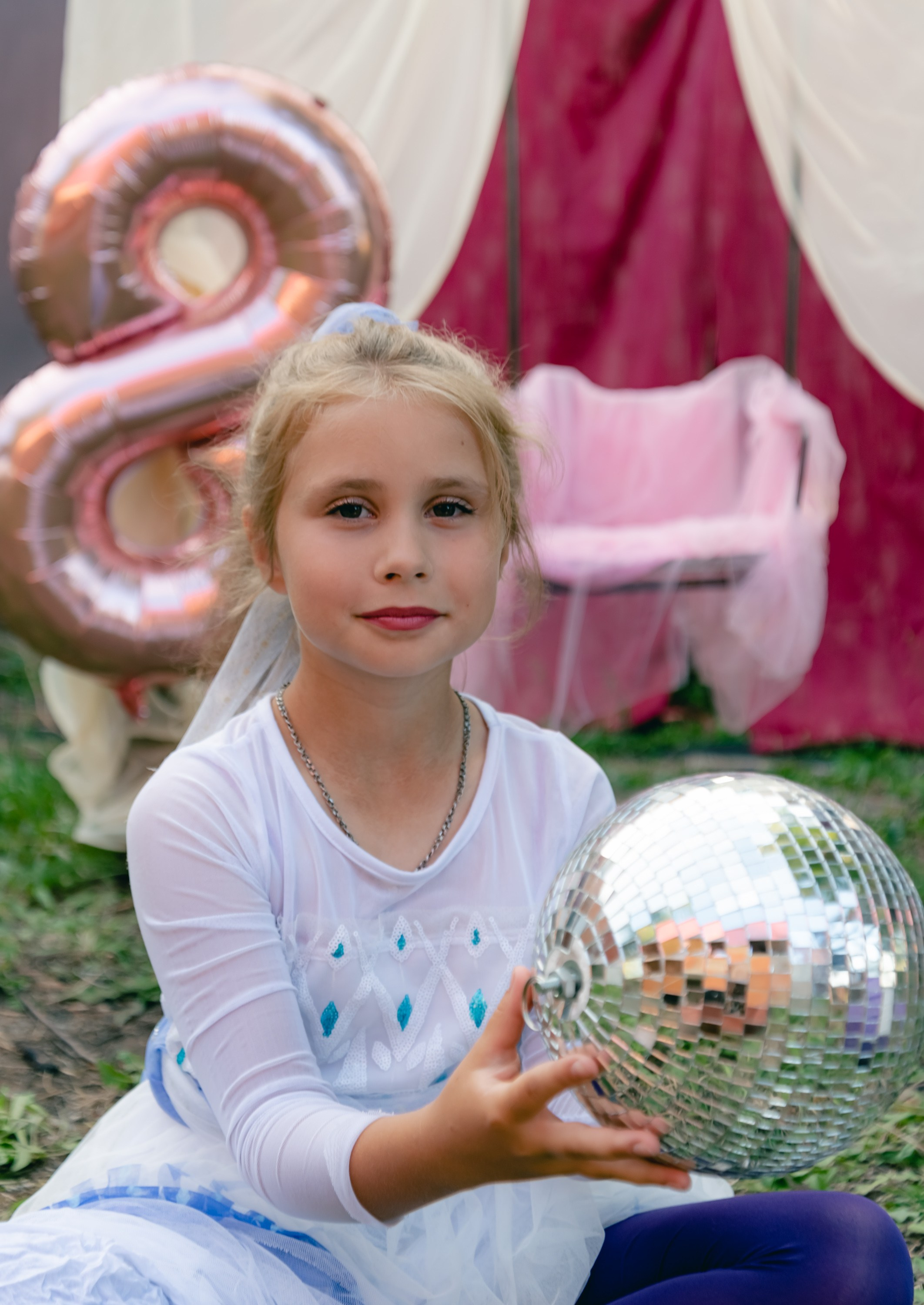 На фото девочка сидит с шариком на земле.