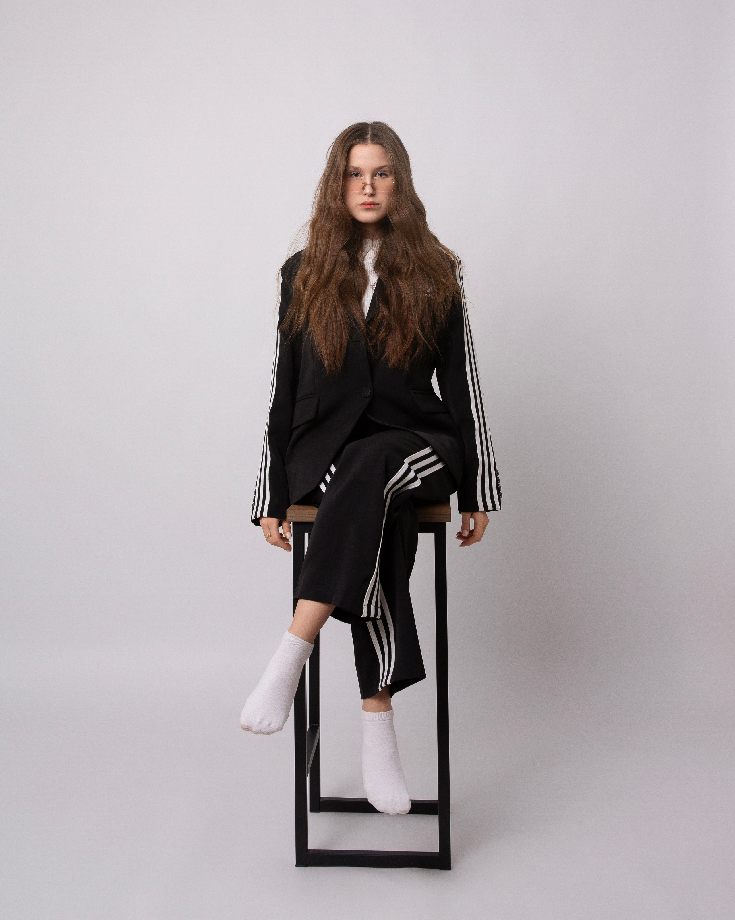 Серьёзная шатенка в спортивном костюме на барном стуле на белом фоне 