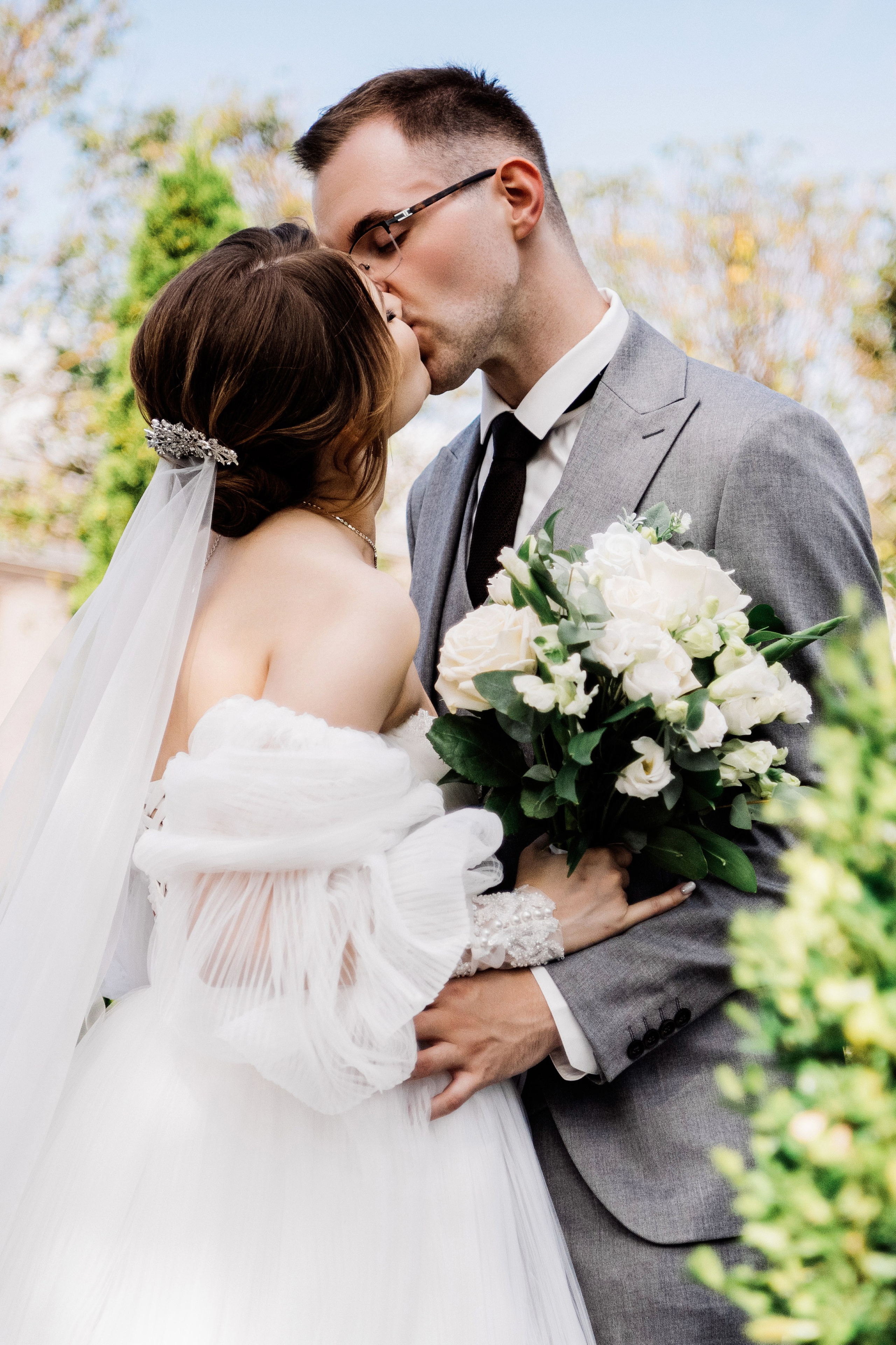 Поцелуй молодожёнов на фоне зелени — романтика в свадебный день