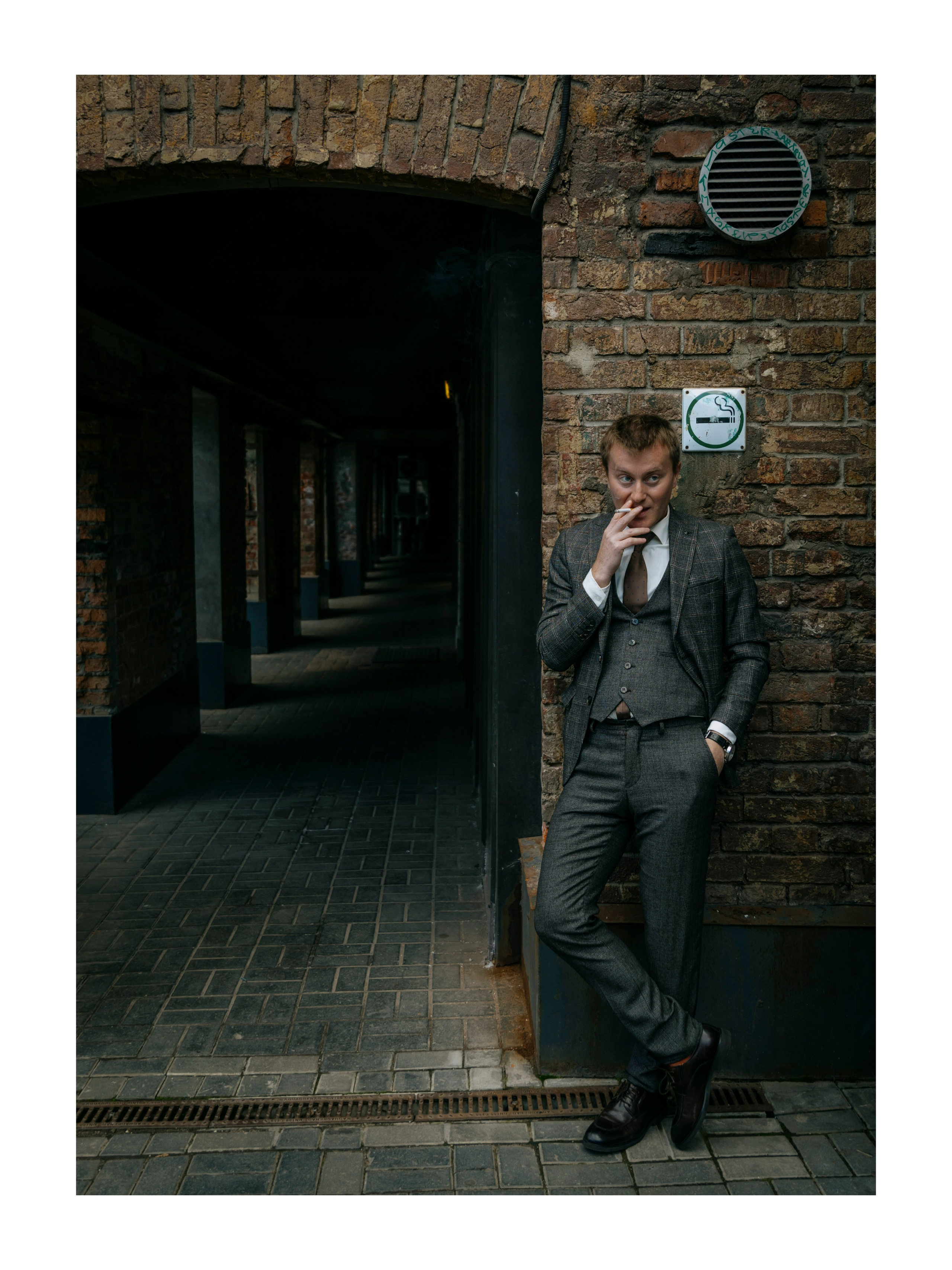 мужчина стоит у кирпичной стены и курит