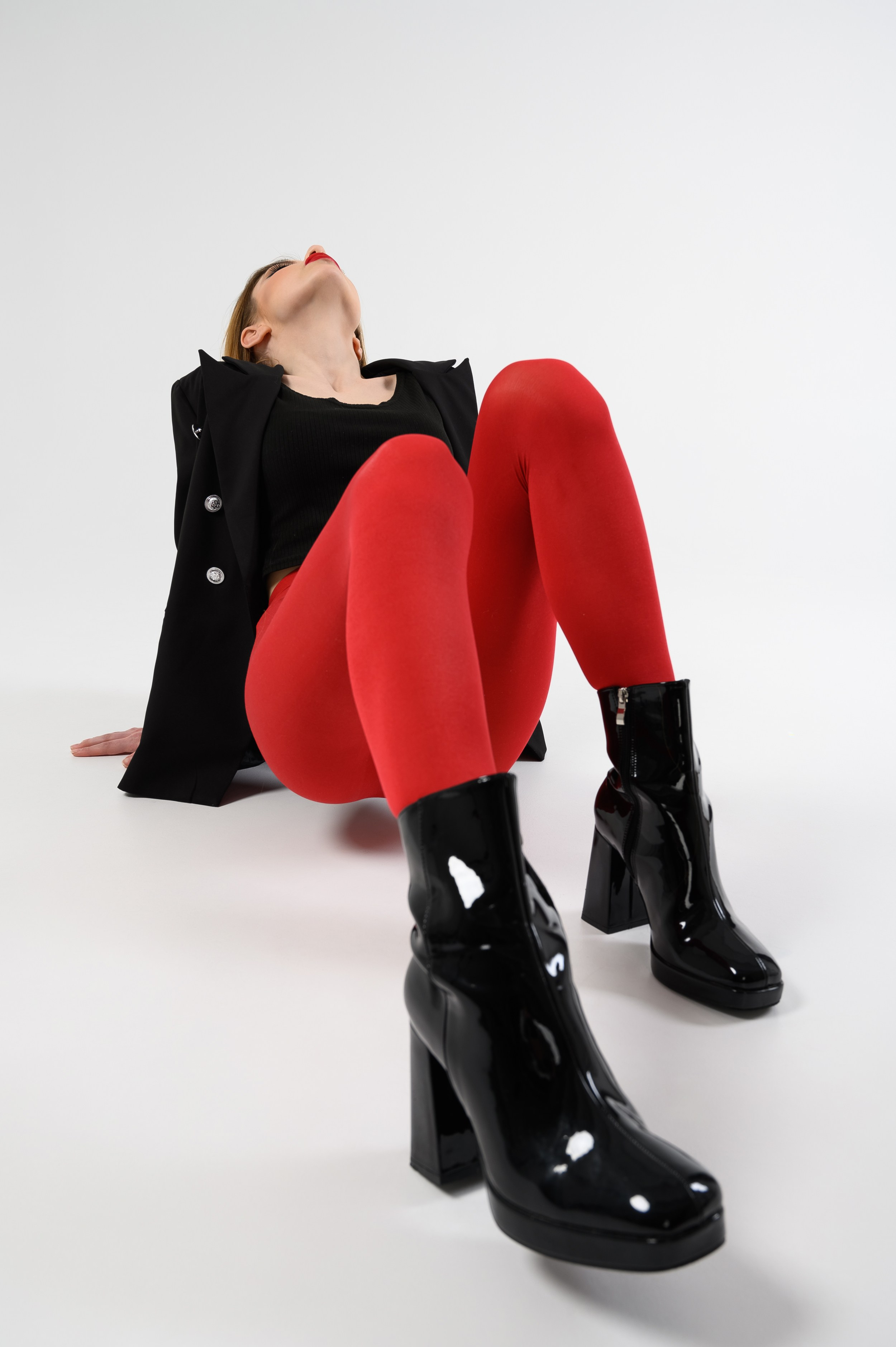 Девушка в красных колготках и черных ботинках в интересной позе ногами к камере в фотостудии