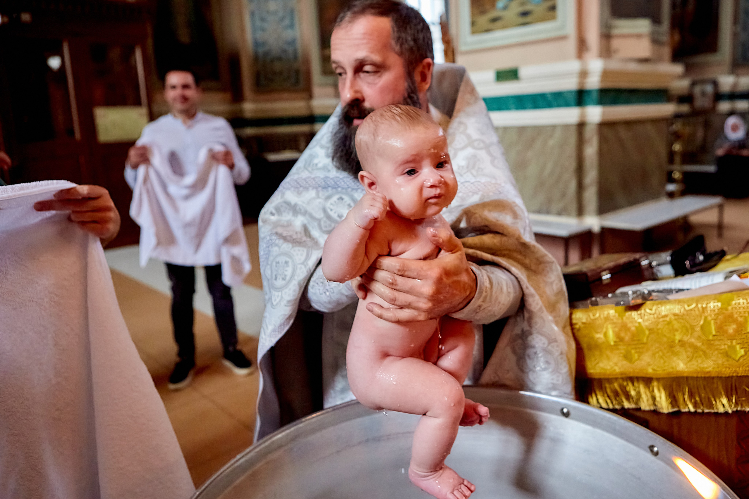 Крестный папа принимает младенца из купели на крещении