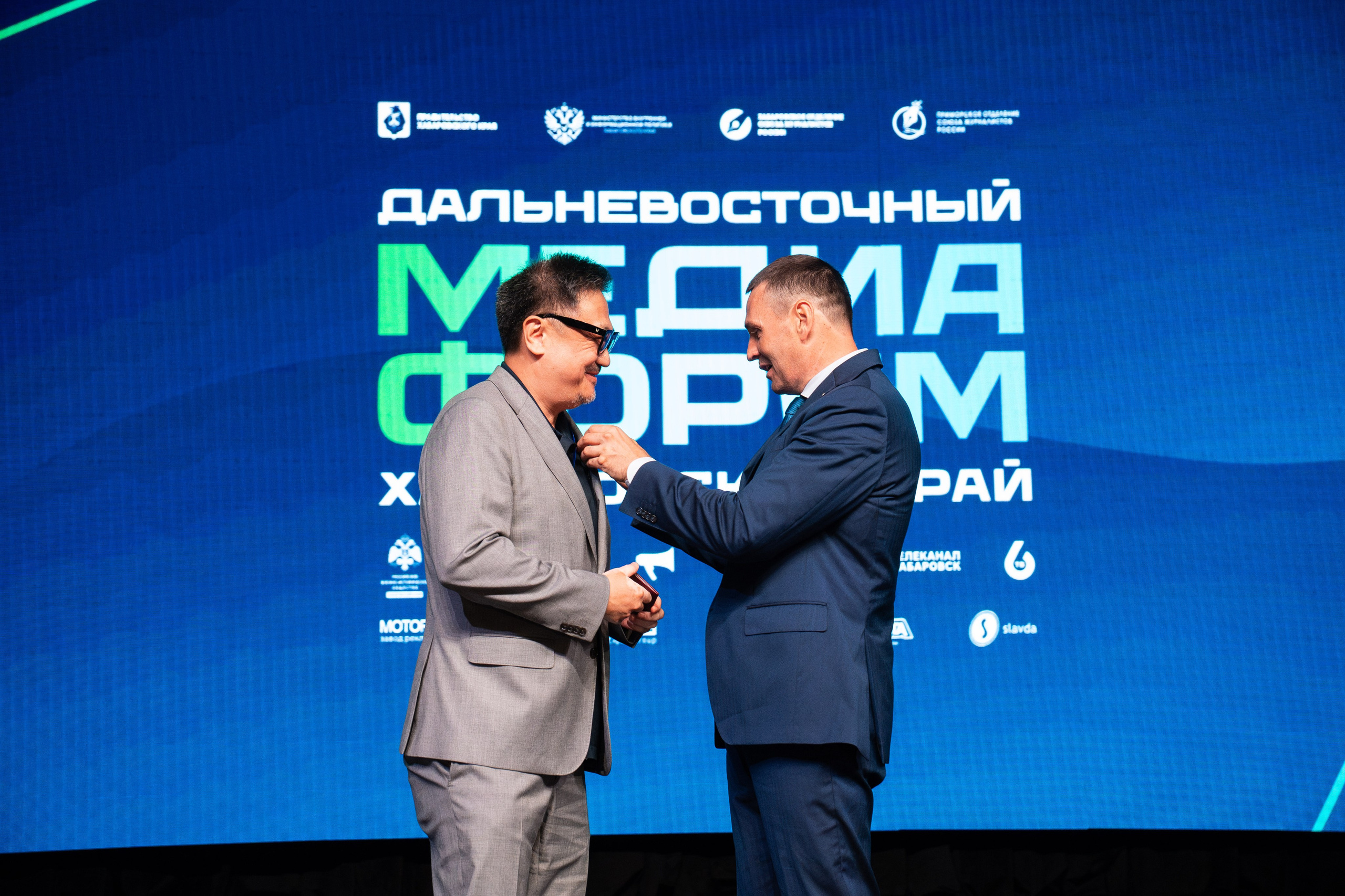 Репортажный фотограф в Хабаровске Дмитрий Дергачев заснял момент вручения нагрудного знака мужчине в сером костюме на сцене Дальневосточного медиафорума.