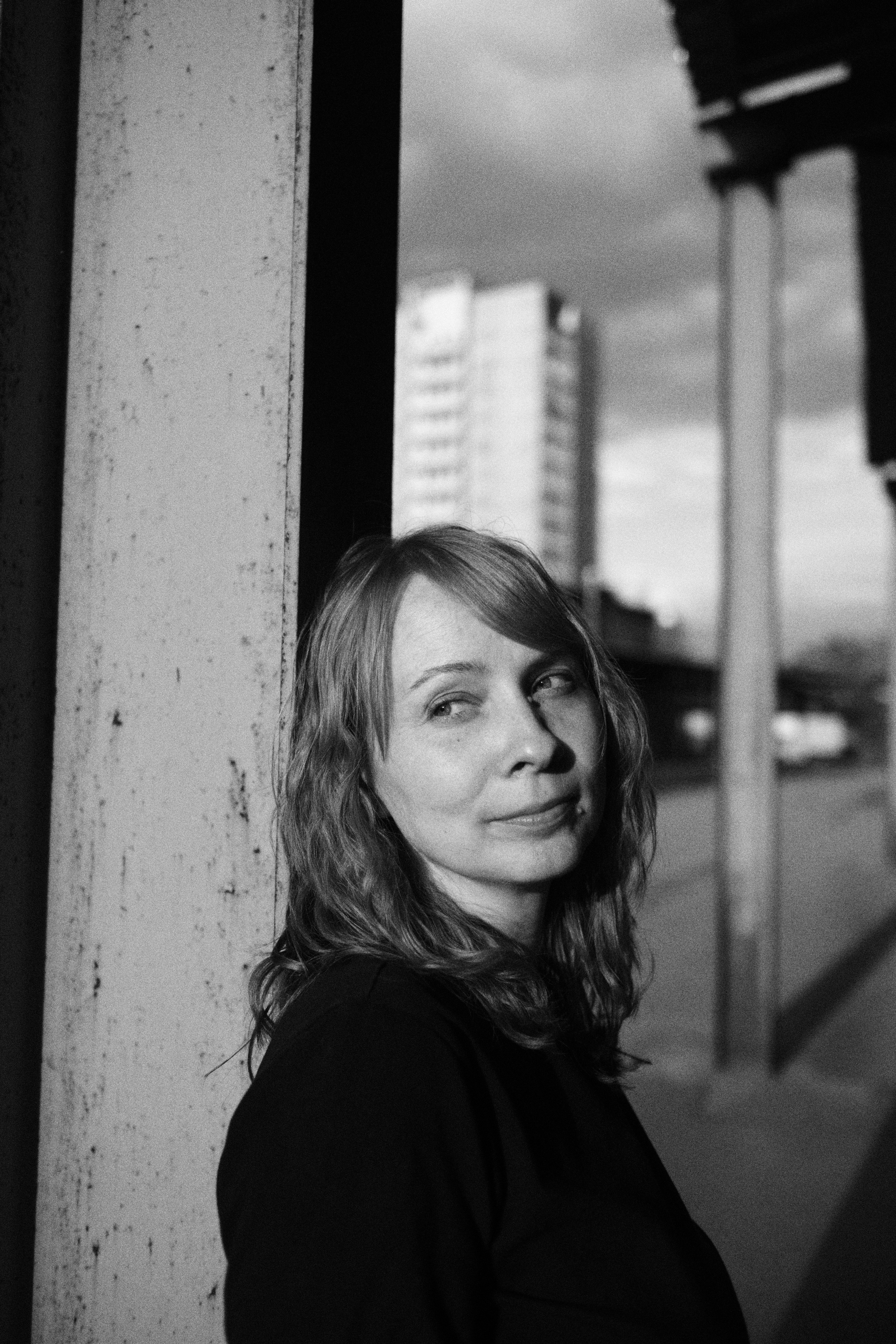 Женщина облокатилась об железную опору, стоит вдаль