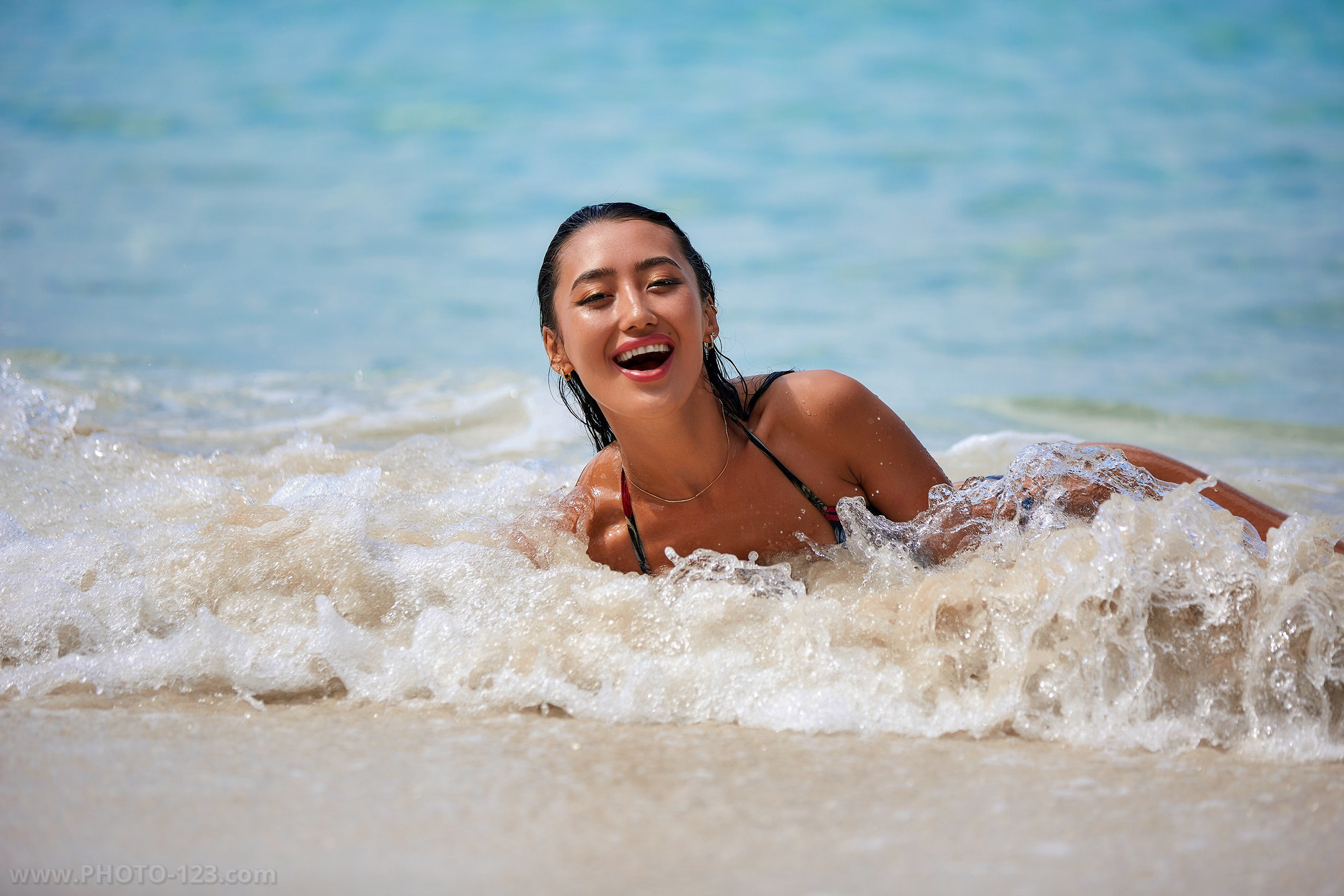 Candid lifestyle portrait of a model laughing in the shallow waves of a pristine Vietnam beach.