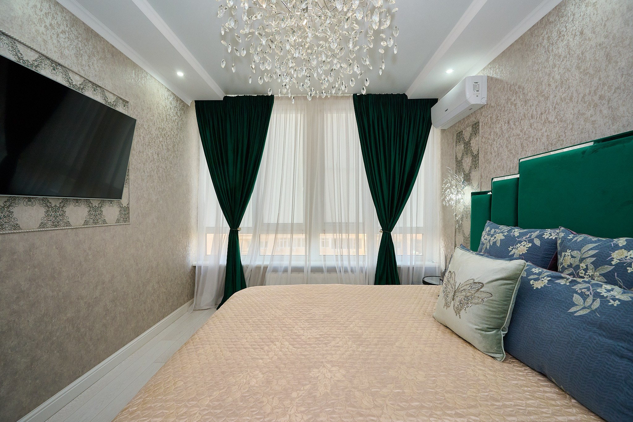 комната светлые стены зеленая кровать зеленые шторы телевизор черный столик 