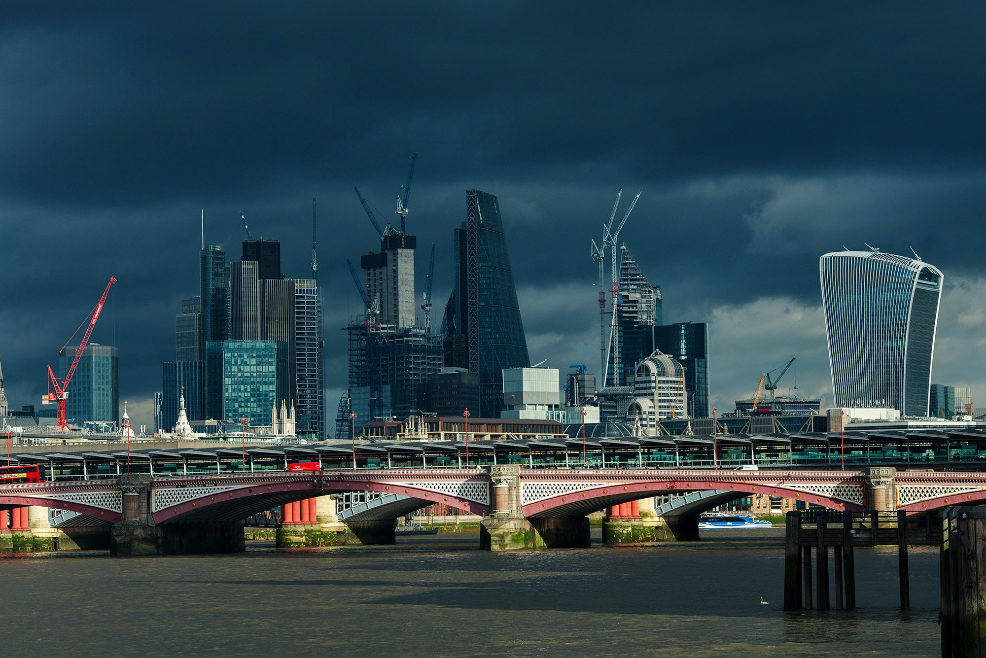 Панорама Лондонского Сити, снятая через арочные пролеты моста Блэкфрайерс-Бридж, на фоне темного грозового неба.