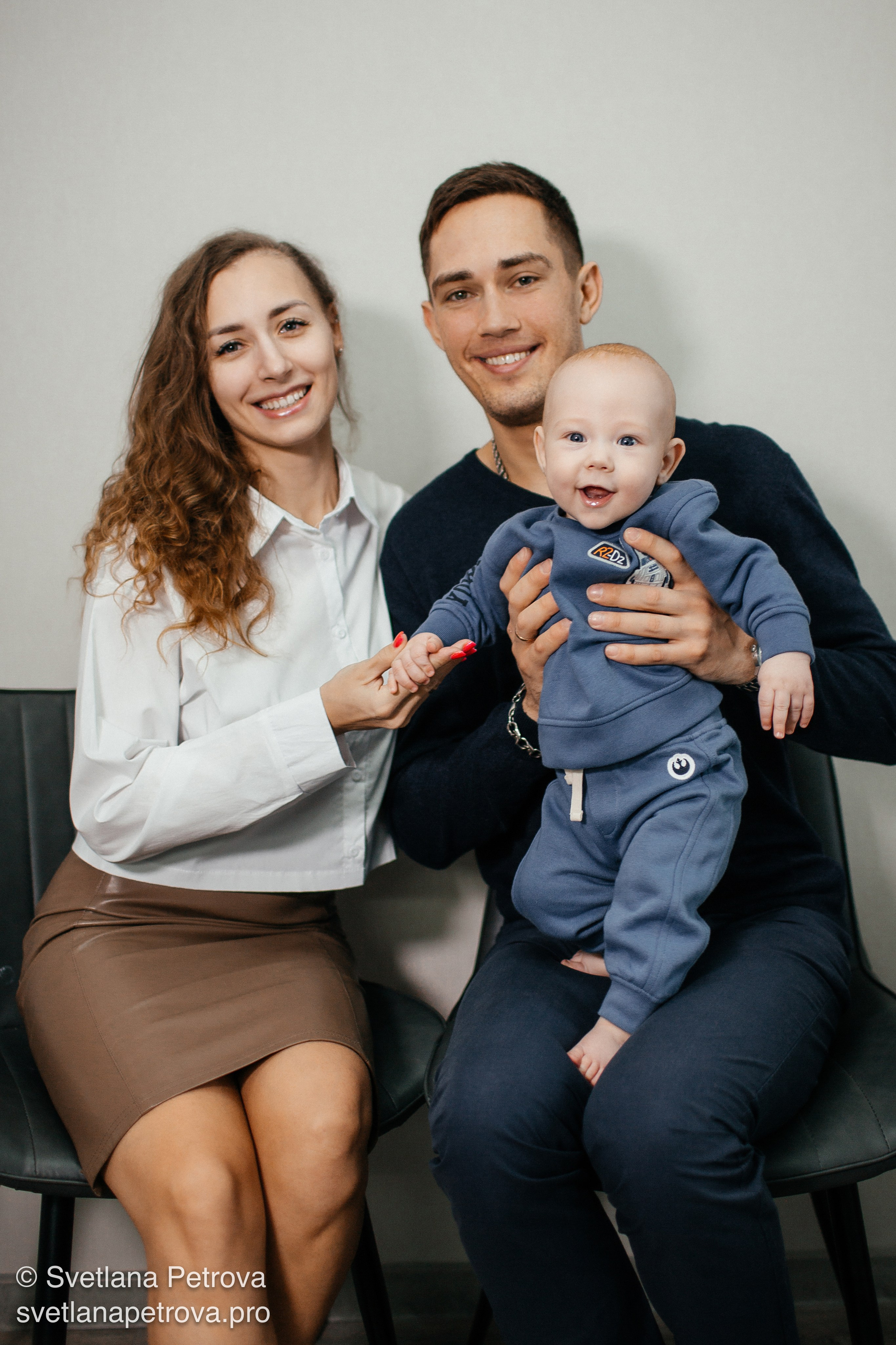 Семейная фотосессия — мама, папа и малыш. Счастливая семья в студии, улыбки на лицах. Родители держат ребёнка, тёплый семейный кадр. Семья из трёх человек, радость в глазах. Мама в белой блузке, папа с малышом на руках. Уютная фотосессия — родители и их кроха. Семья дома: любовь, смех, гармония.