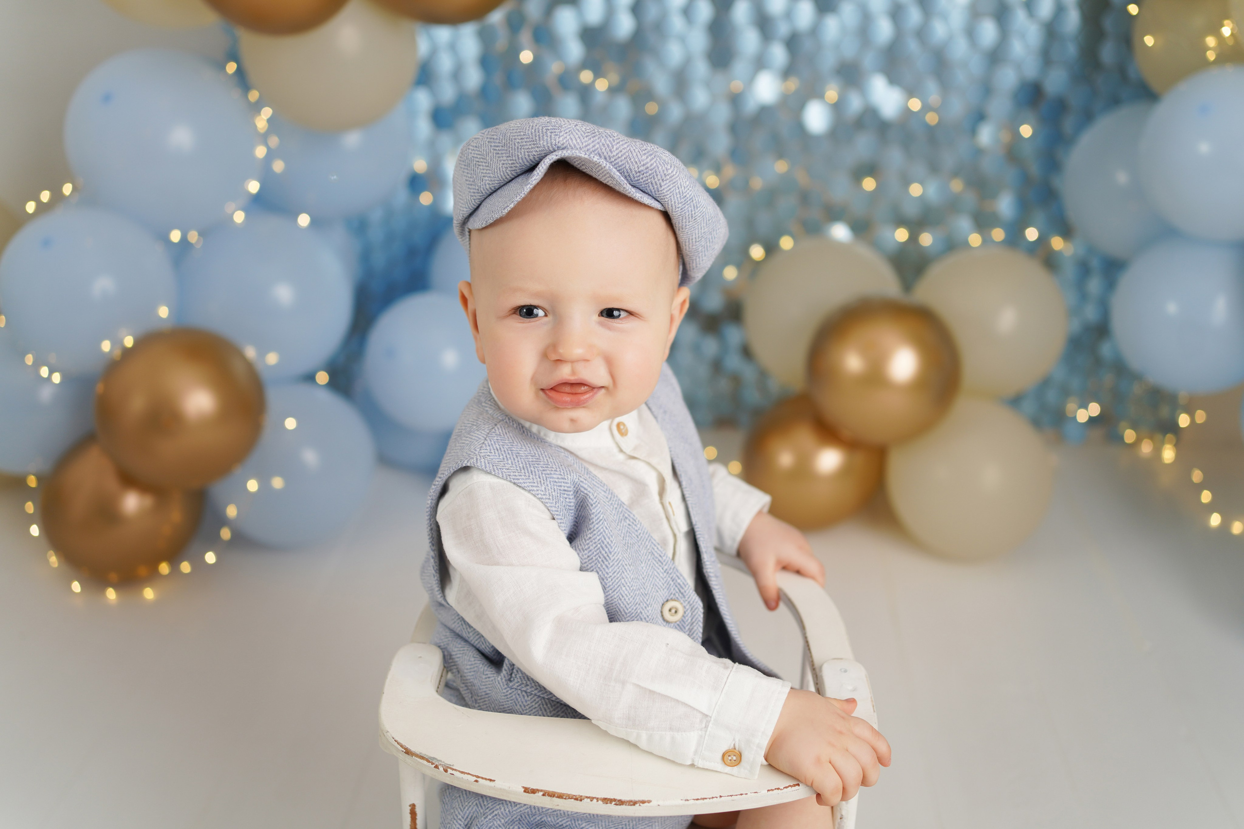 На фото улыбающийся малыш в нарядной голубом костюме и кепочке.
