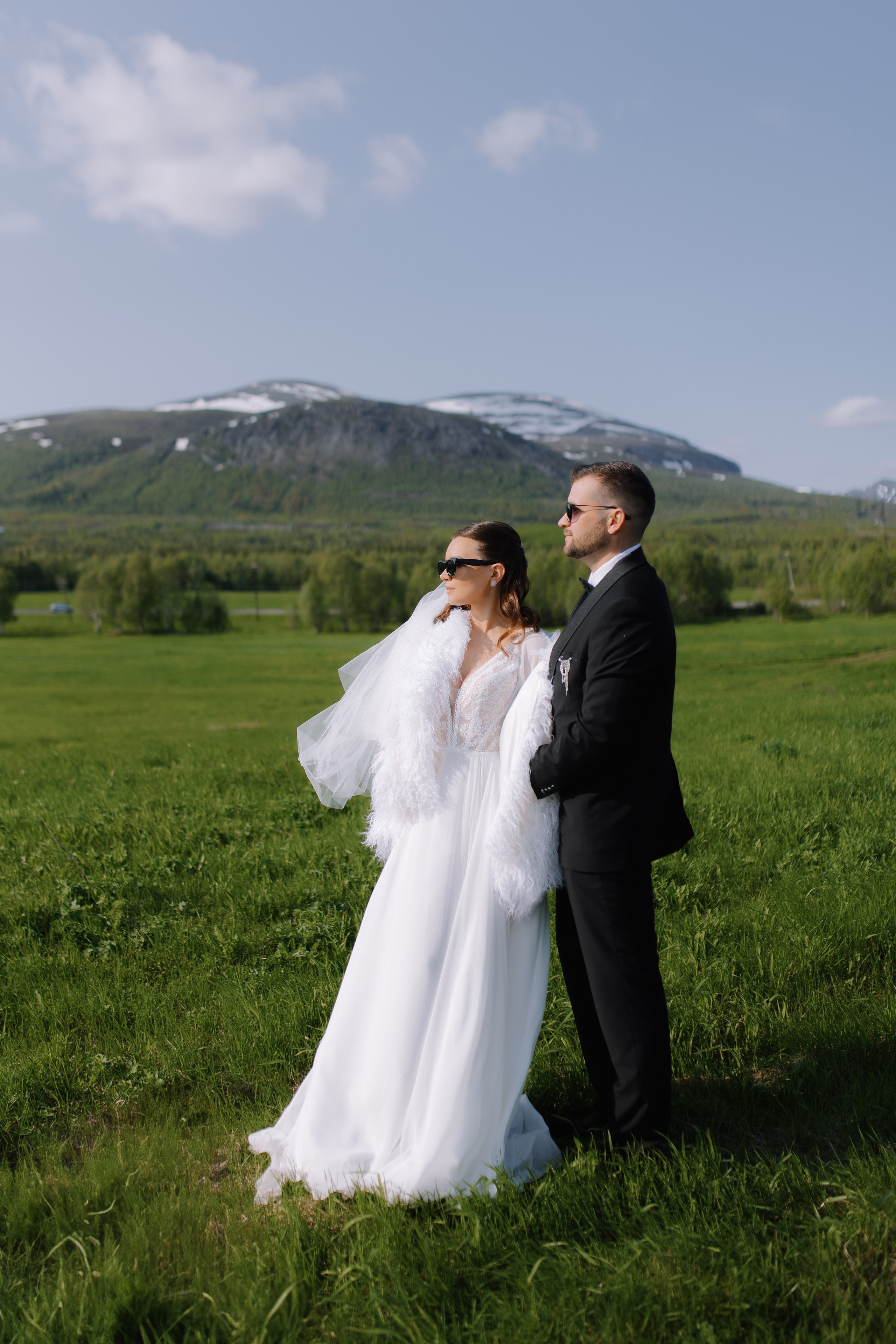 Обручённые руки с кольцами на фоне высокогорного озера под ясным небом.