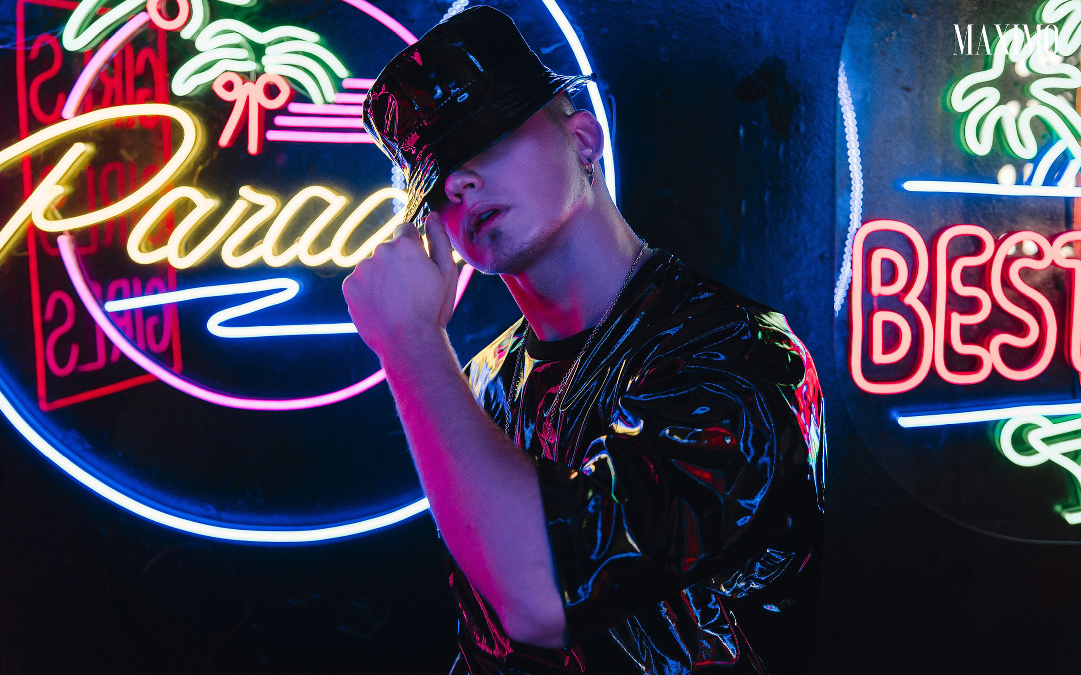 Накаченный мужчина в черной шляпе на фоне неонового света.