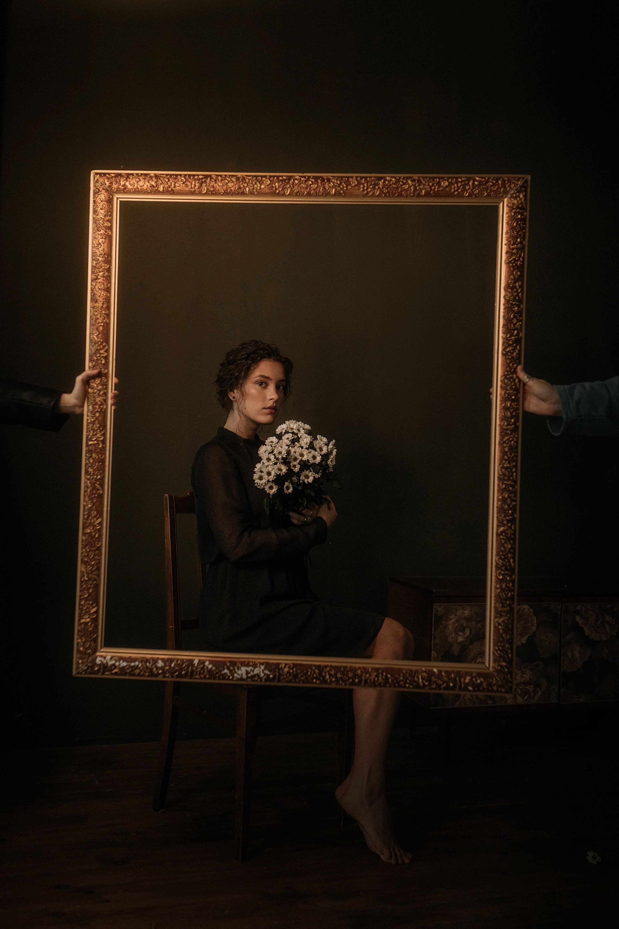 Женщина с цветами в руках элегантно позирует в богато украшенной рамке на темном фоне в креативной художественной обстановке