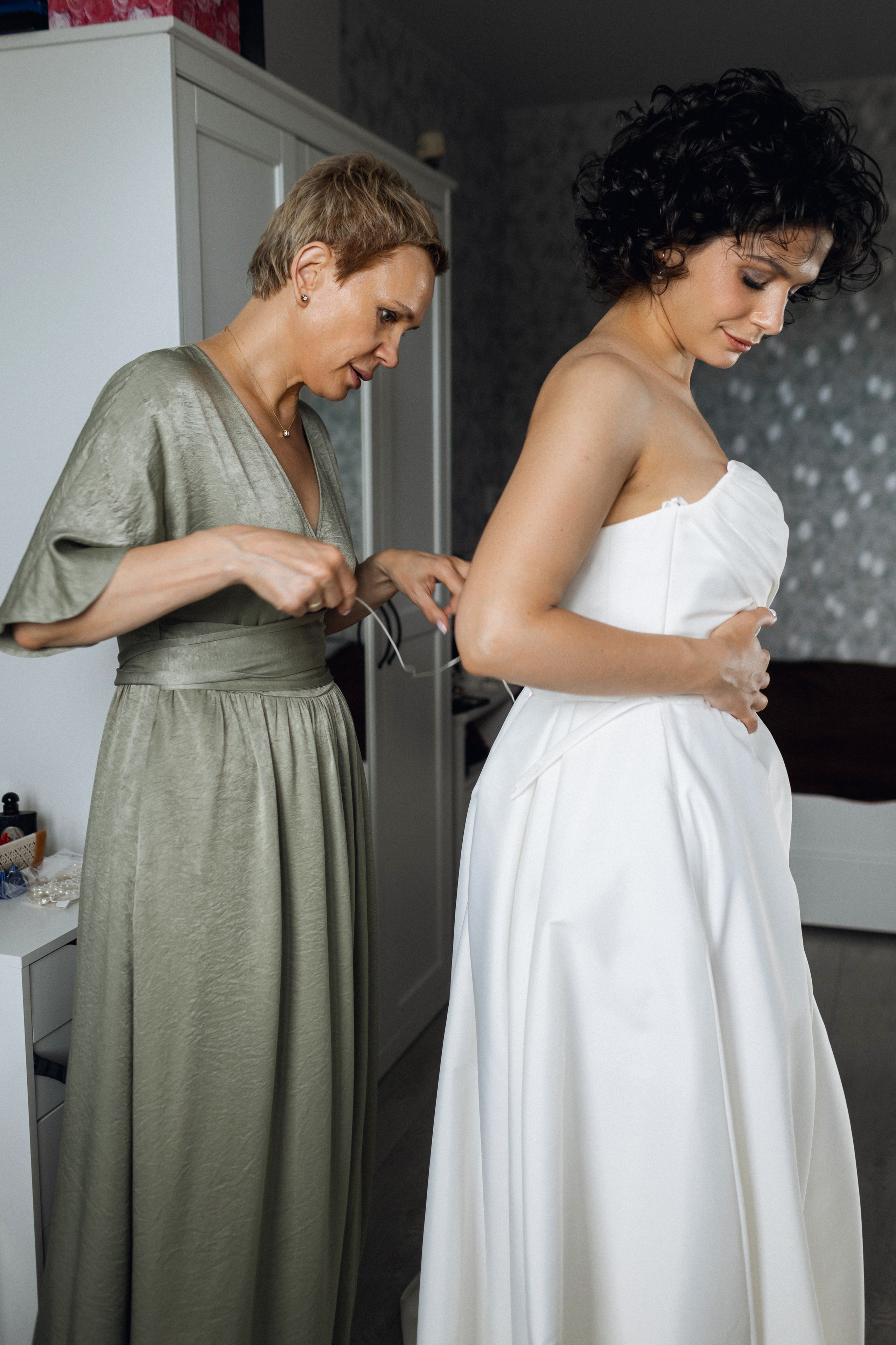 Ностальгия и эстафета поколений: невеста в свадебном платье от салона NATALIE L которое нежно шнурует мама на спине своей дочери 