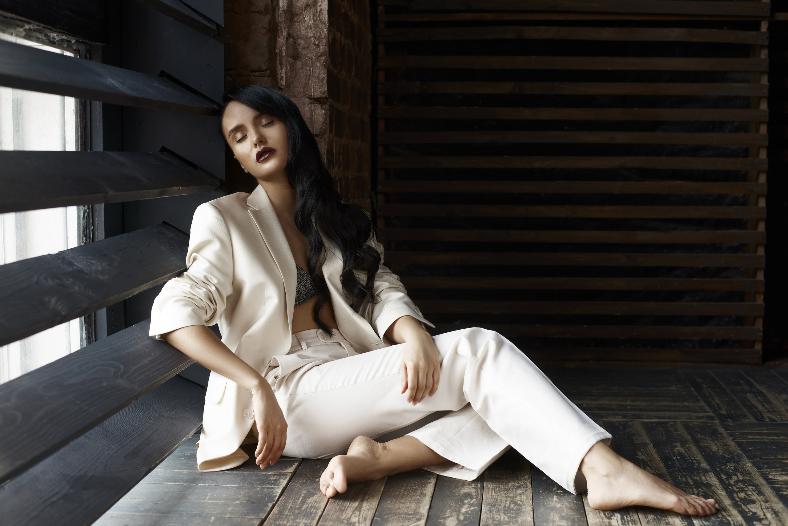 Фотосессия в брючном костюме белого цвета на полу босой темноволосой девушки 