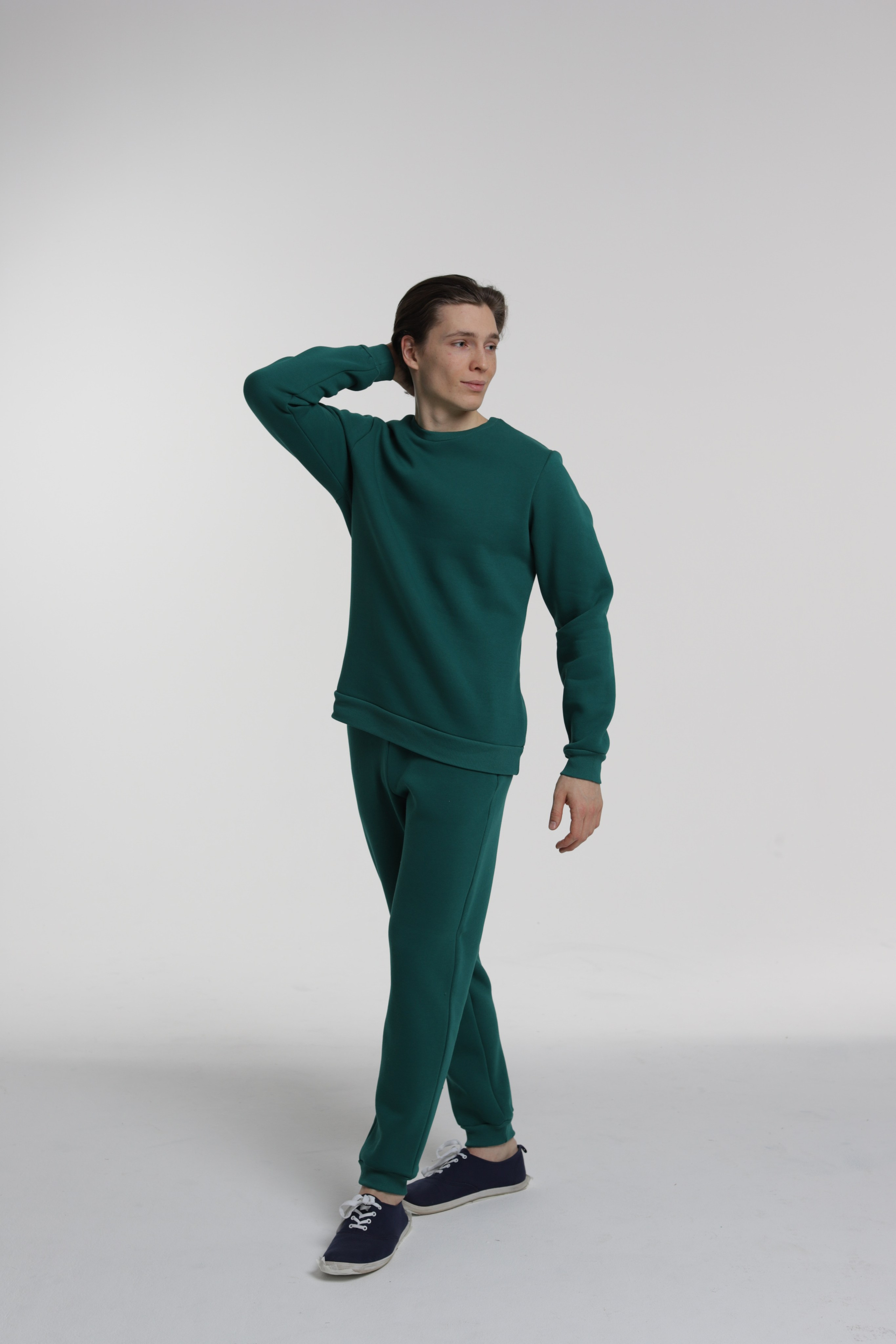 Парень модель в зеленой одежде позирует на циклораме