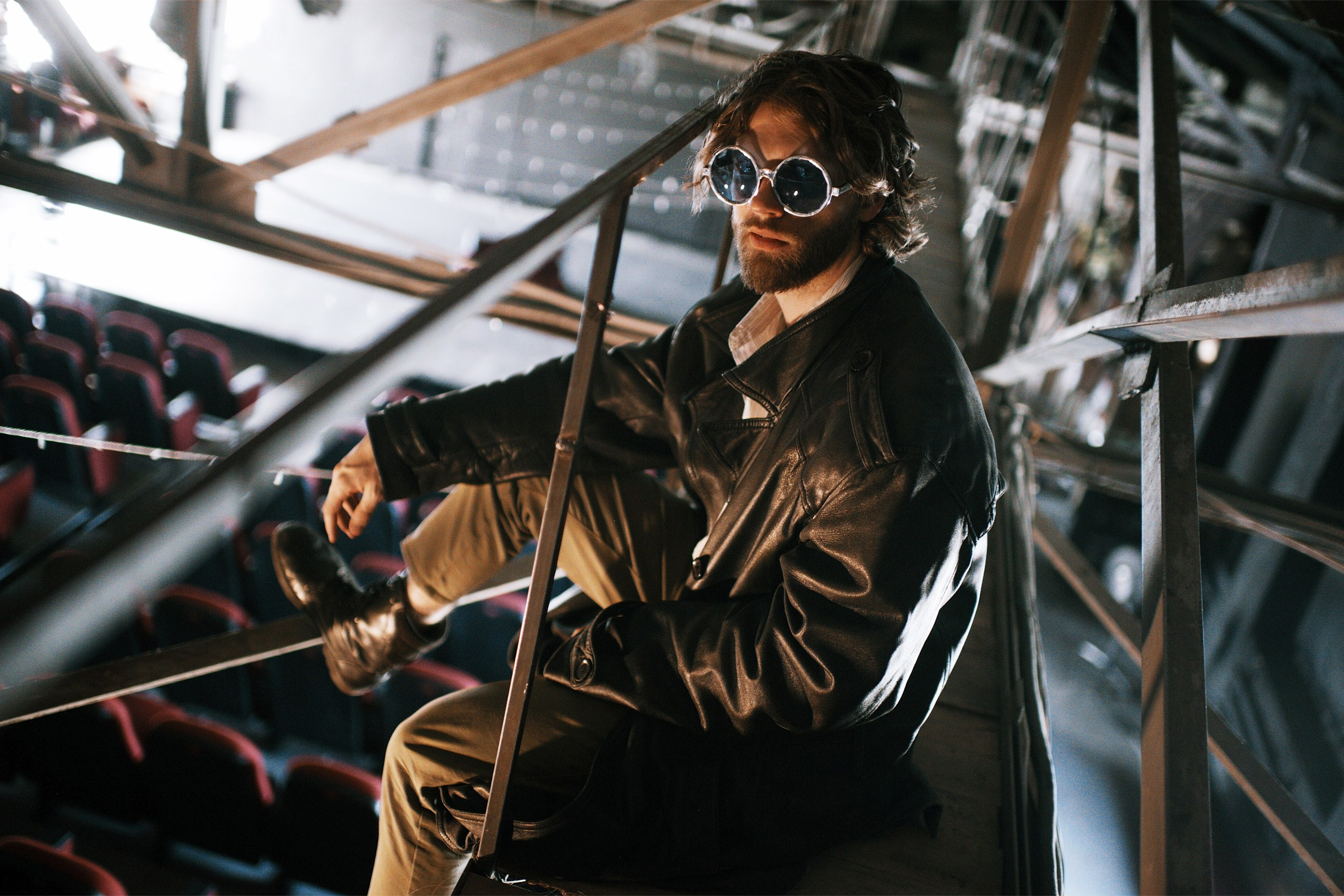 Парень в солнечных очках в кожаном плаще сидит под крышей зрительного зала