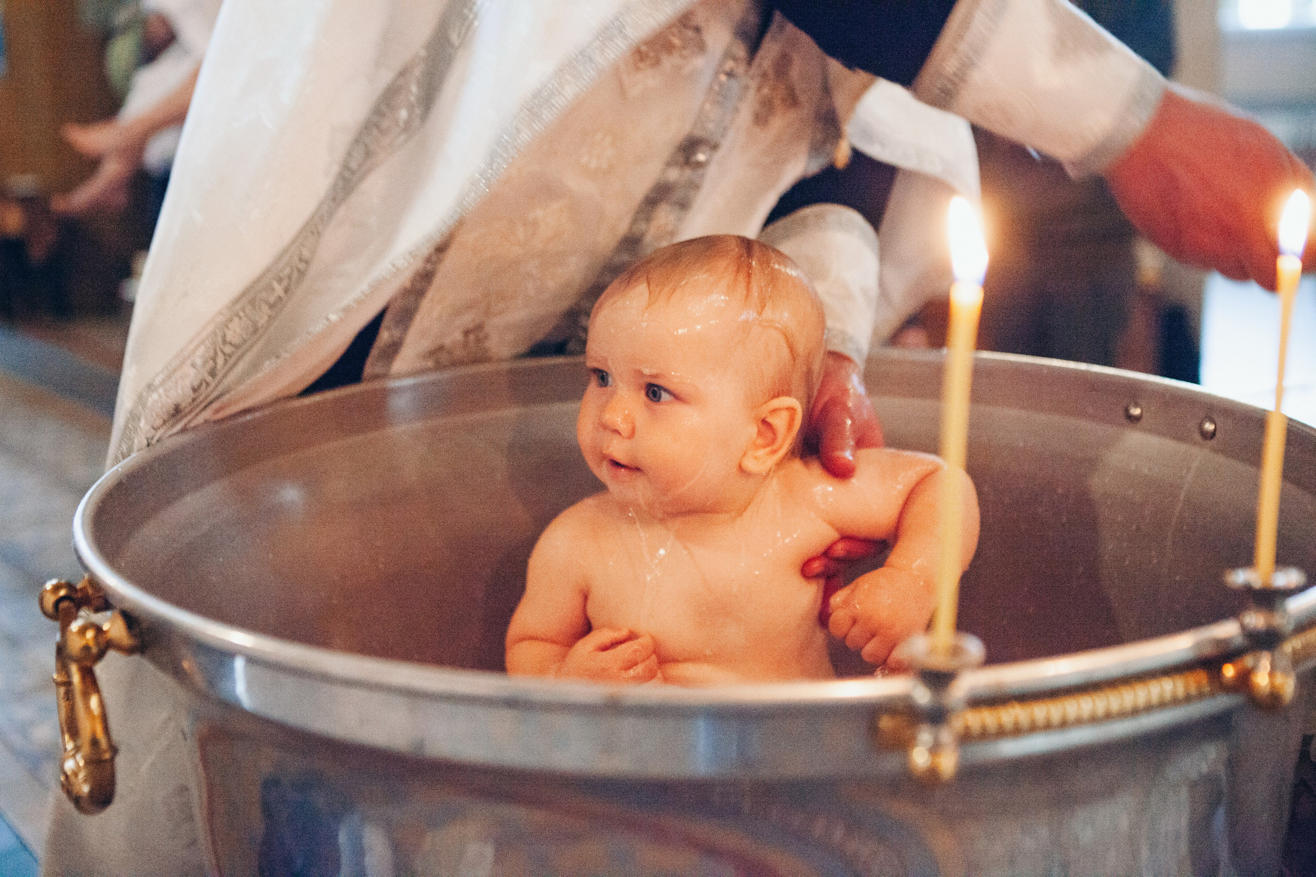 малыш в купели проходит обряд крещения при свечах