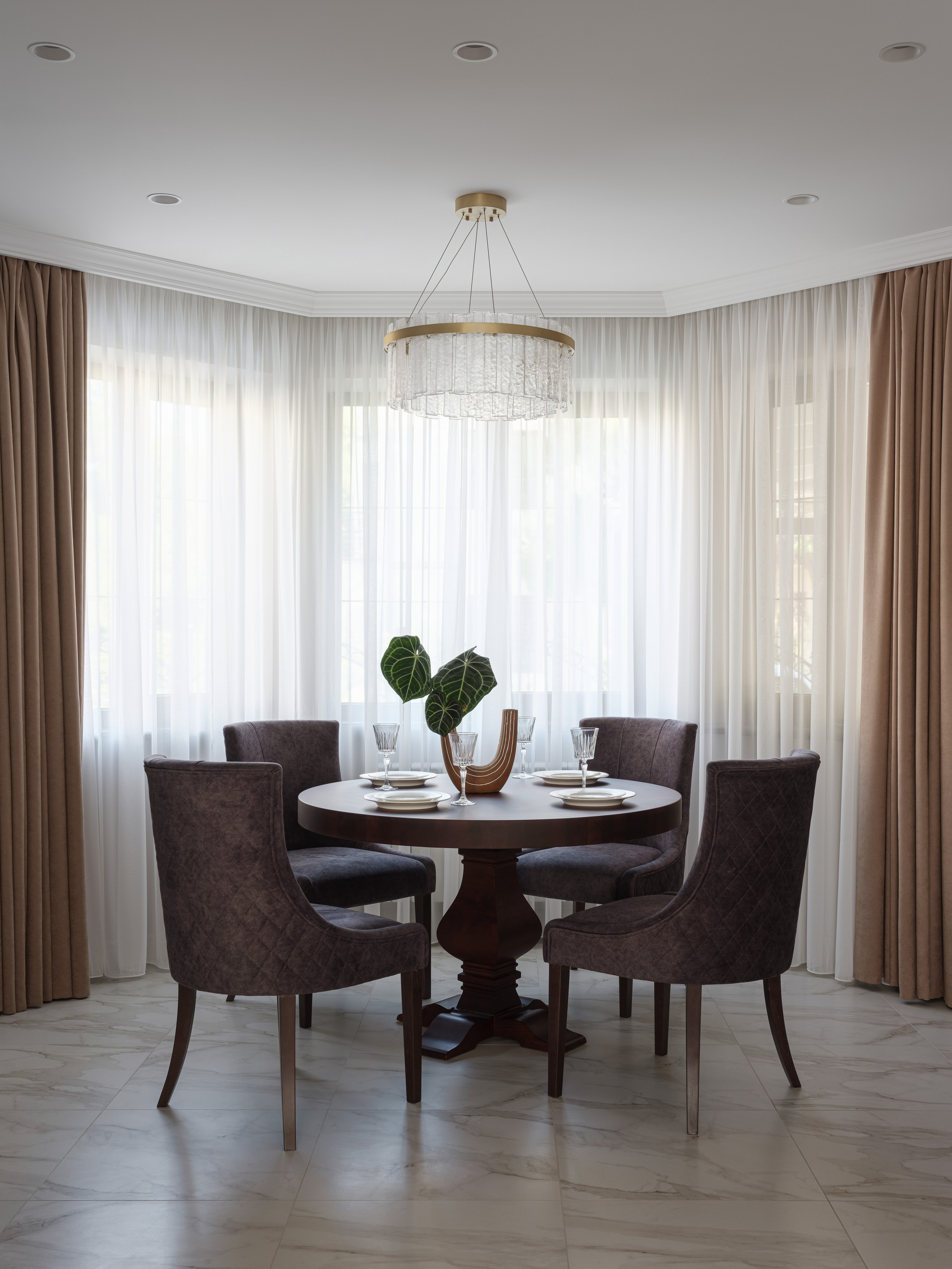 Уютный современный интерьер столовой с круглым деревянным столом, мягкими стульями и изысканной люстрой, оформленный в светлых тонах. Автор проекта Татьяна Диденко, фотограф Сергей Денисенко, стилист Наталья Якушева.