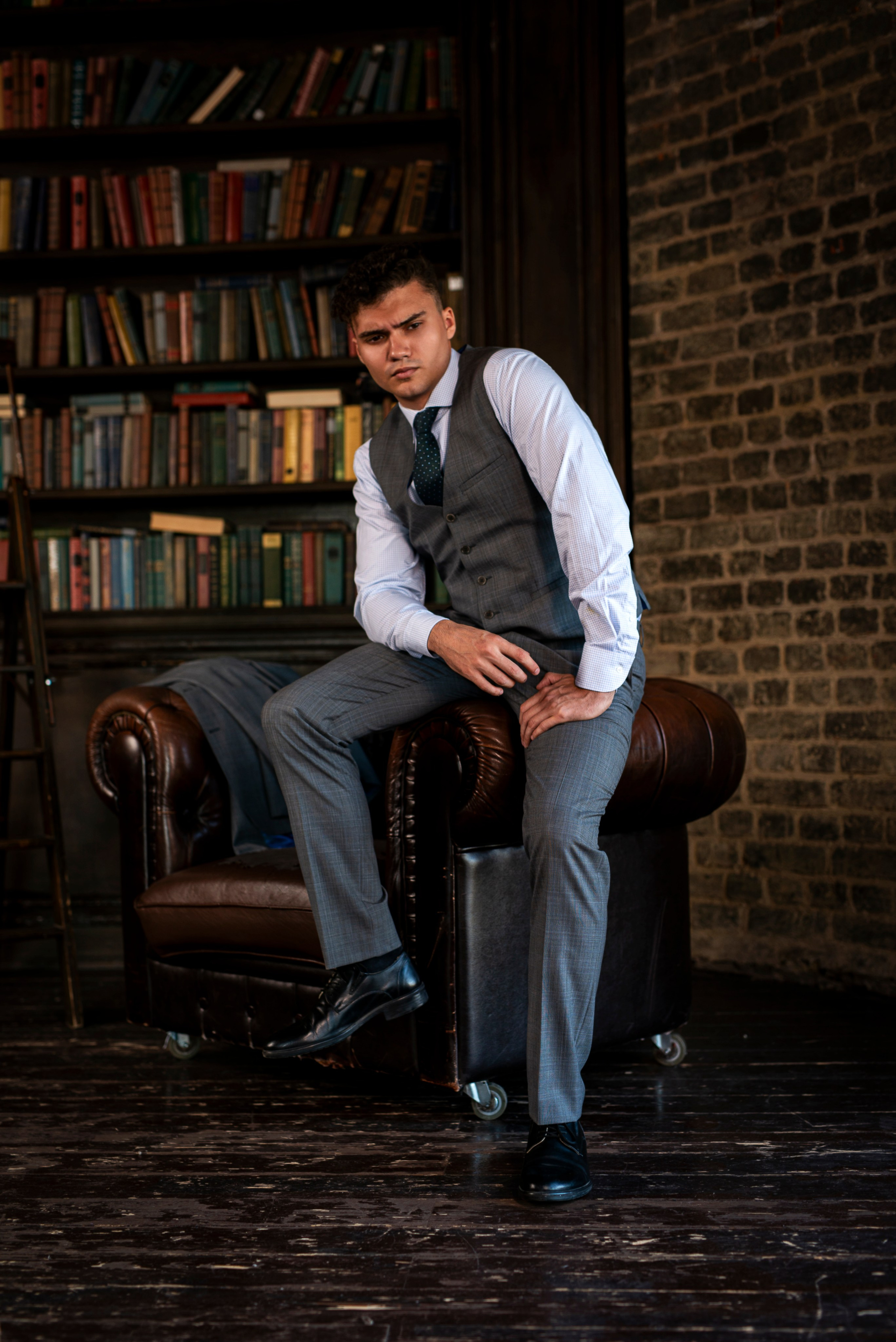 Во время съёмок мужчина, одетый в костюм, расположился на краю кресла.