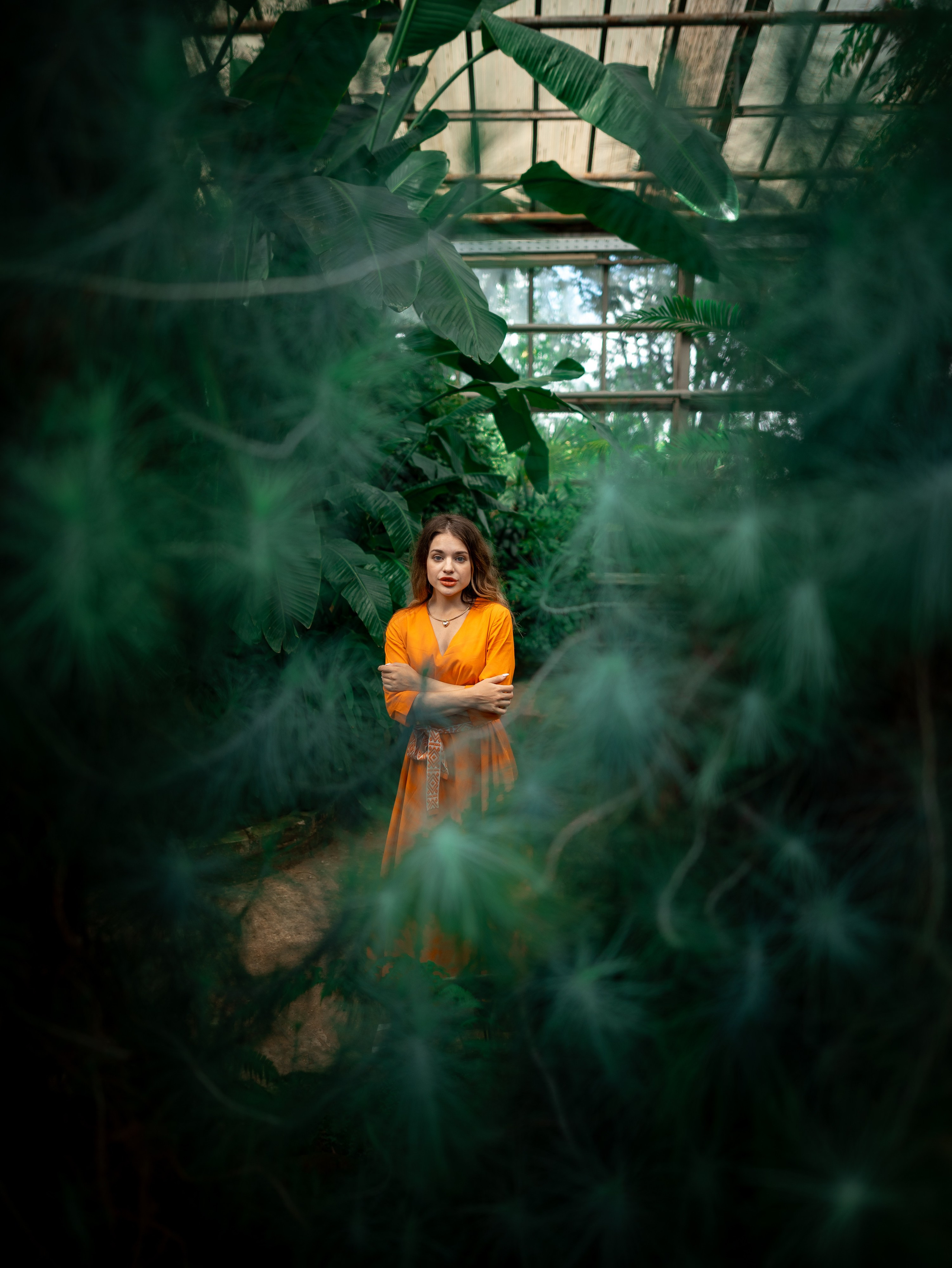 Девушка в оранжевом платье стоит на фоне зелени