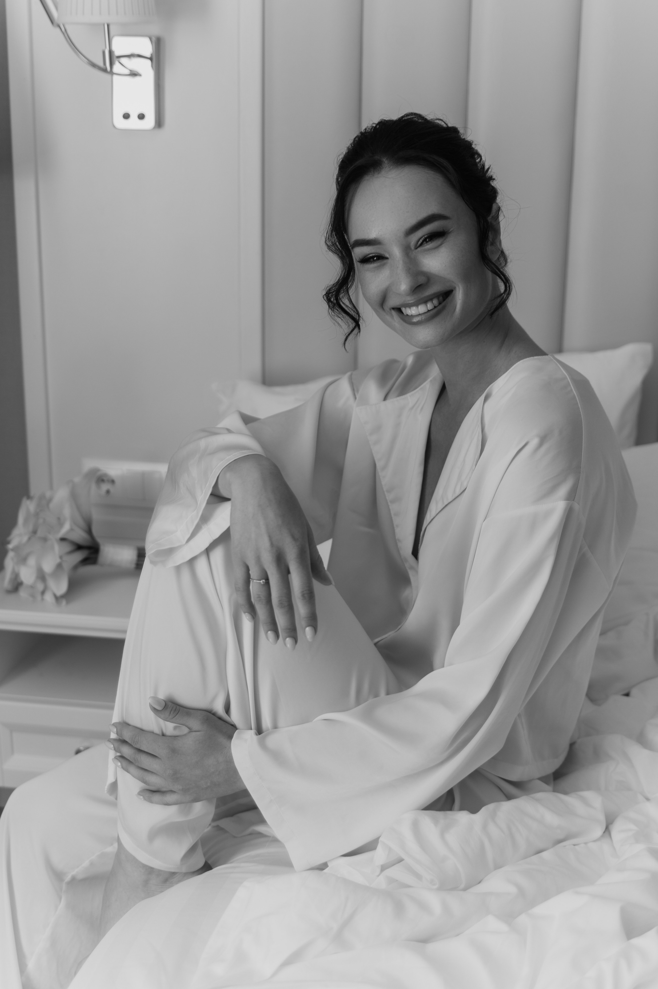 Свадебный фотограф в Твери: фотосессия в отеле утро невесты, невеста сидит на кровати и позирует с нежной улыбкой