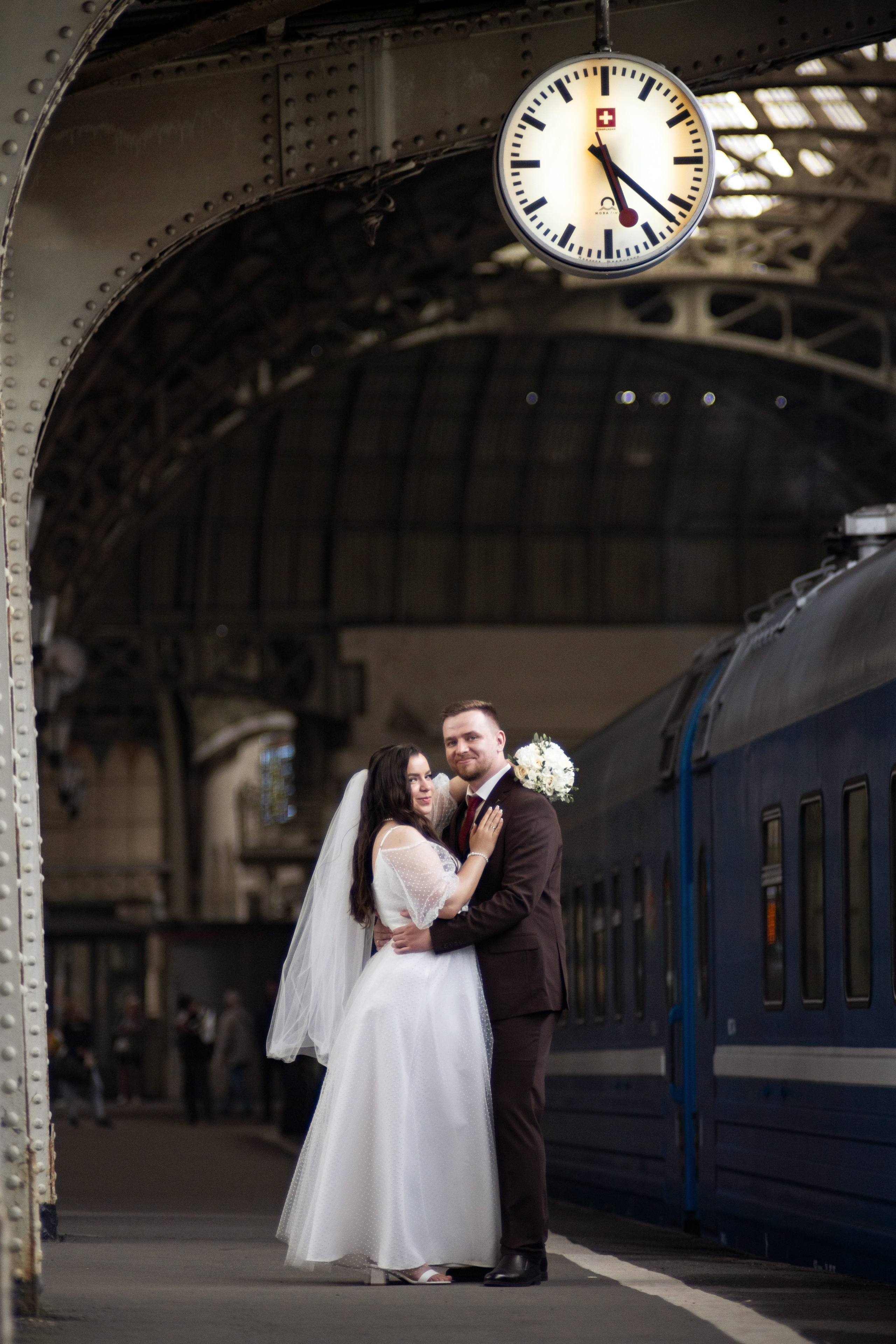 Свадебная фотография на Витебском вокзале в Санкт-Петербурге Жених и невеста обнимаются на перроне под часами