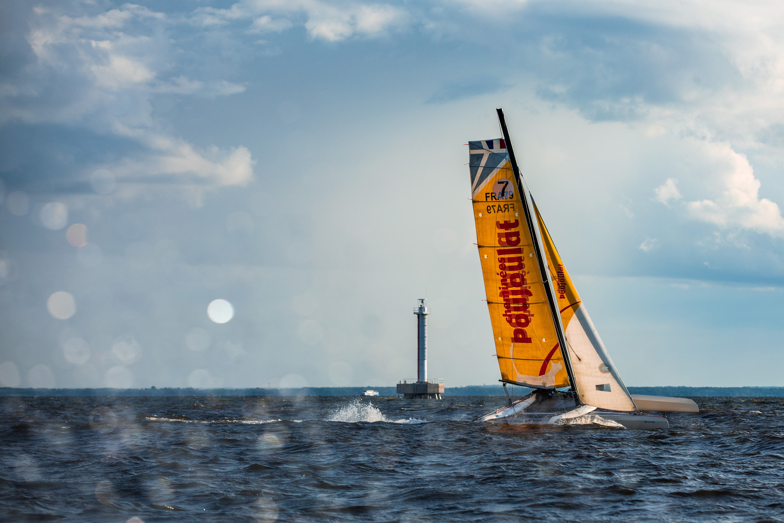 Парусный тримаран на фоне маяка на регате в Санкт-Петербурге.