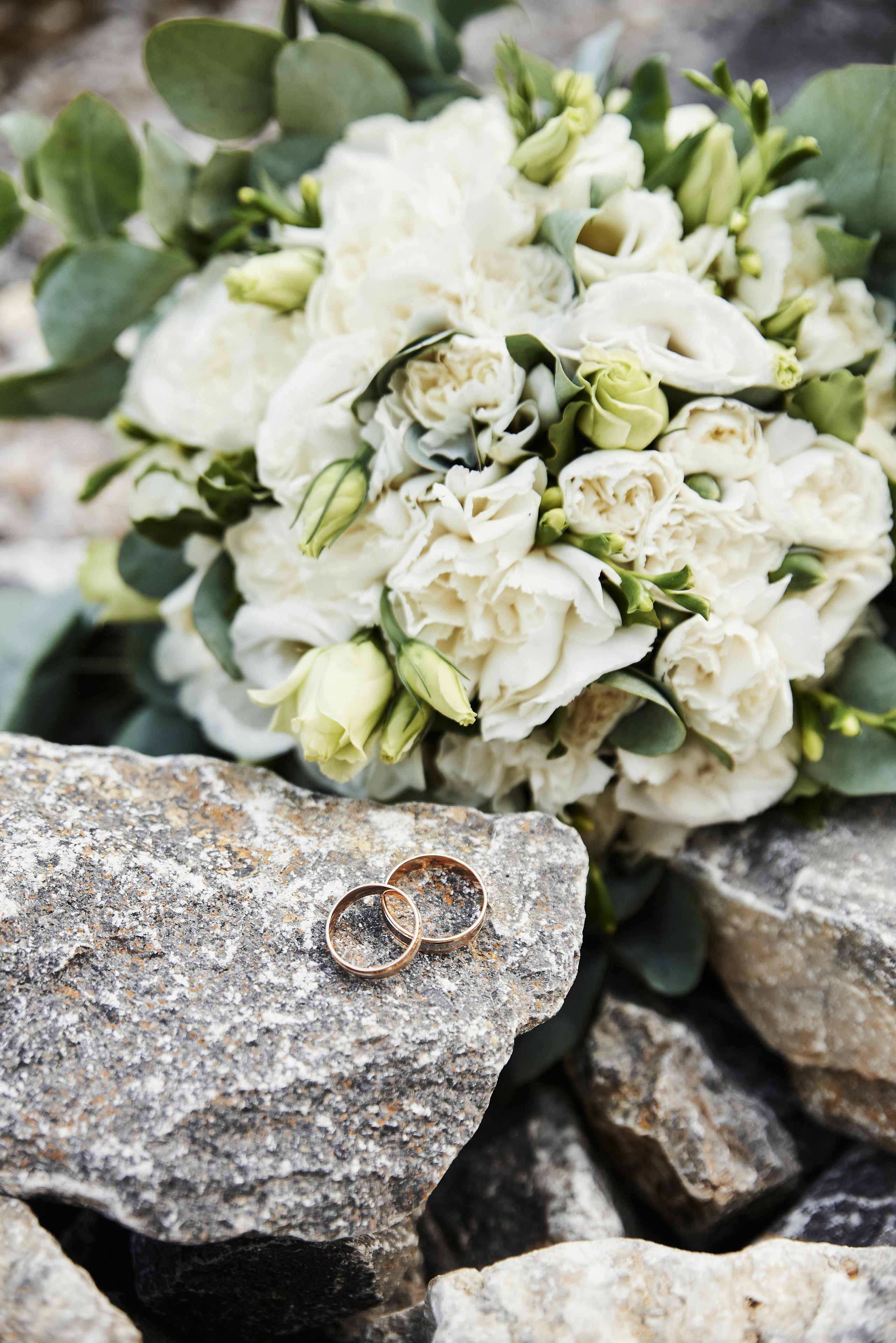 Обручальные кольца лежат на камнях рядом с букетом невесты